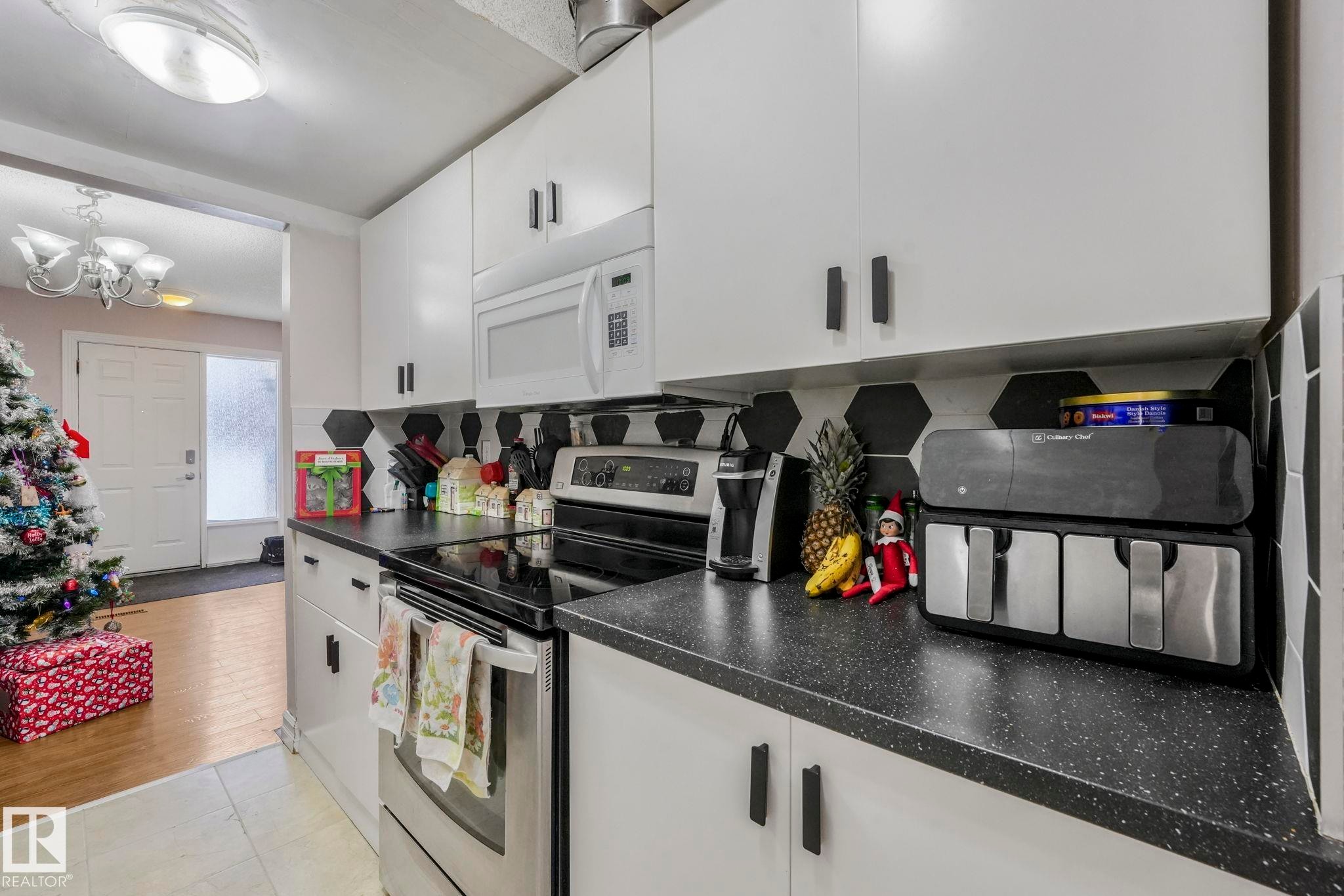 Kitchen with electric range, white microwave, white cabinetry, dark countertops, and decorative backsplash - 11811 32A Avenue, Edmonton, AB - Indoor Photo Showing Kitchen