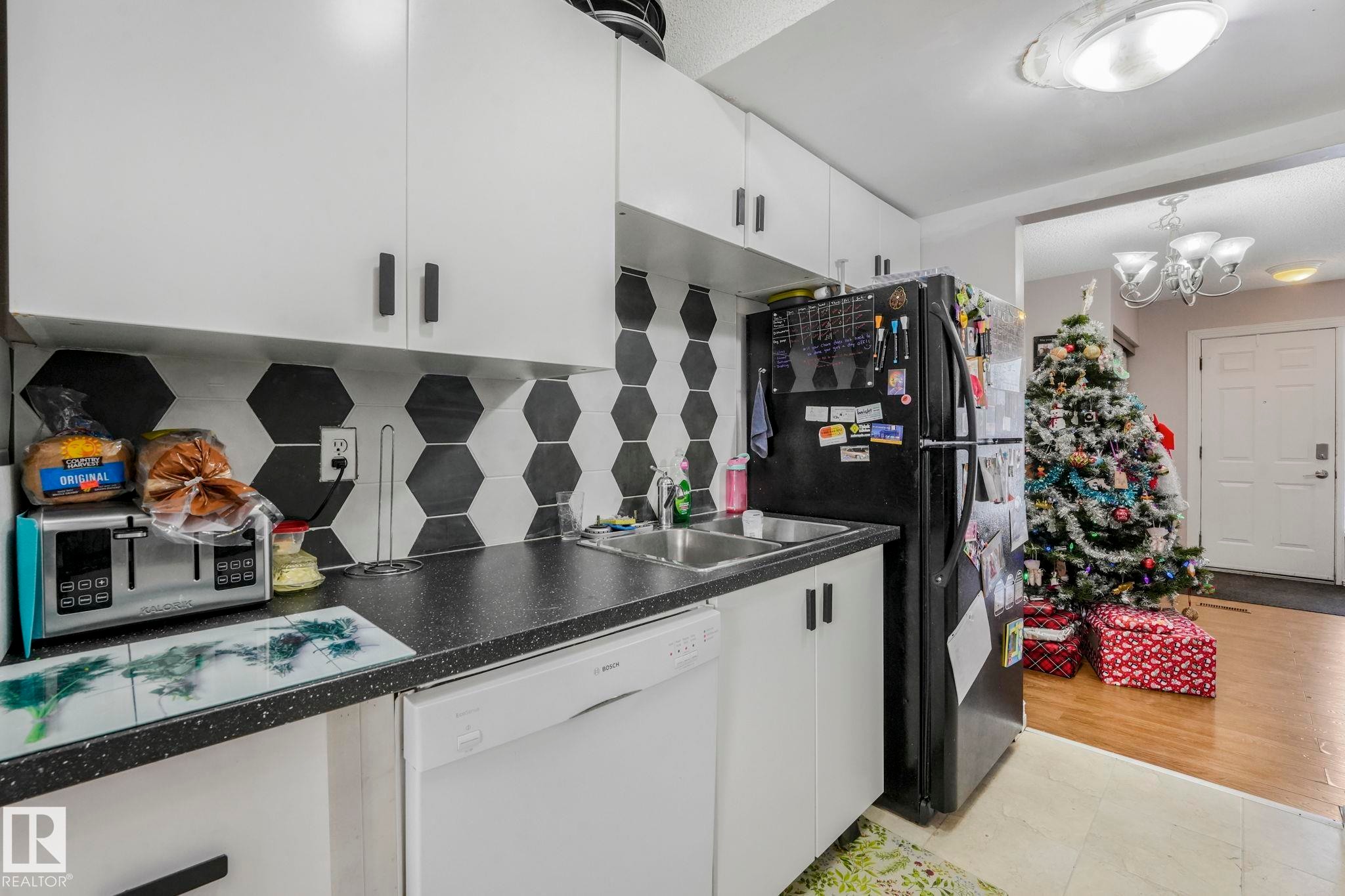 Kitchen featuring dishwasher, white cabinetry, freestanding refrigerator, dark countertops, and tasteful backsplash - 11811 32A Avenue, Edmonton, AB - Indoor Photo Showing Kitchen With Double Sink