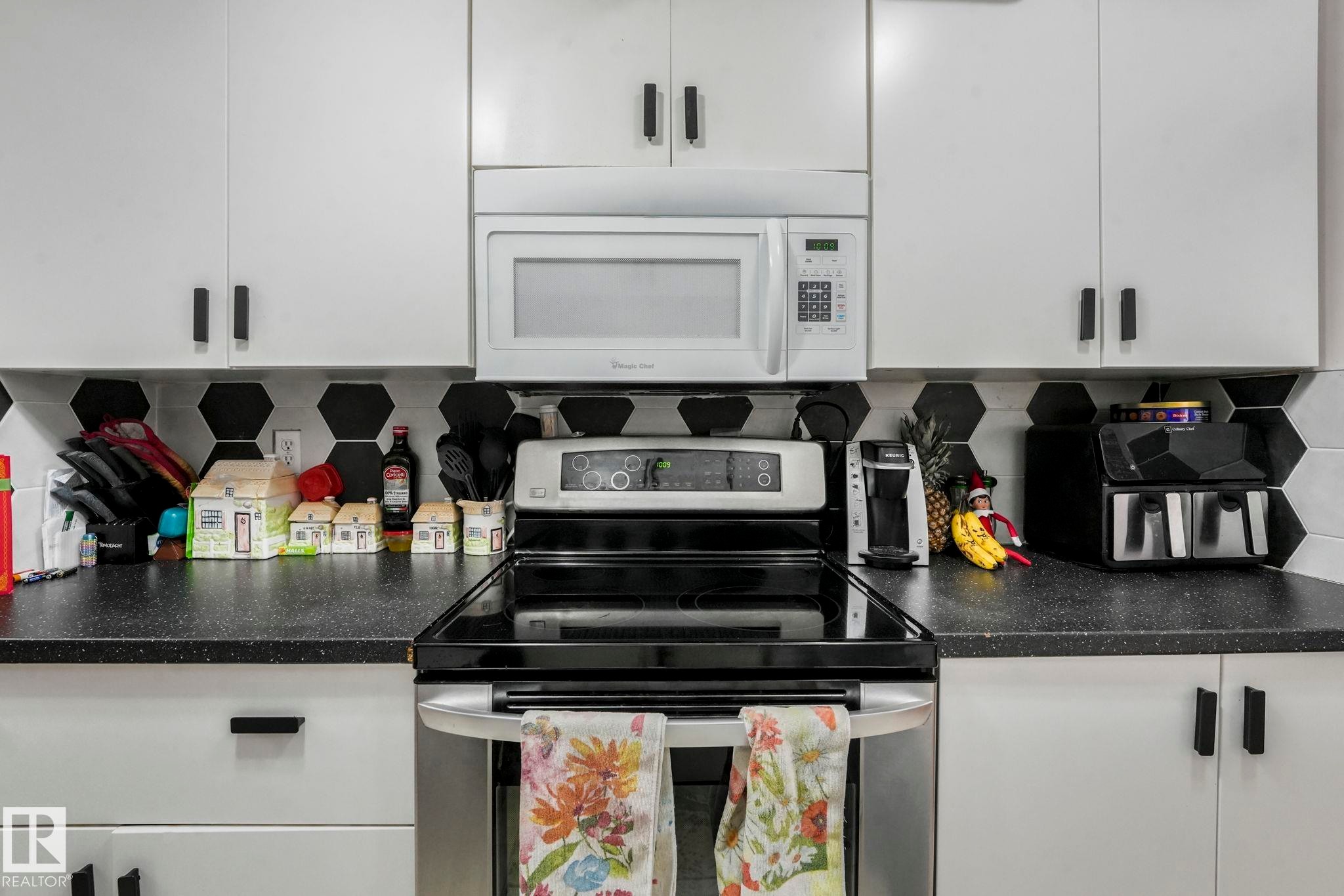 Kitchen featuring stainless steel electric stove, dark countertops, decorative backsplash, and white microwave - 11811 32A Avenue, Edmonton, AB - Indoor Photo Showing Kitchen