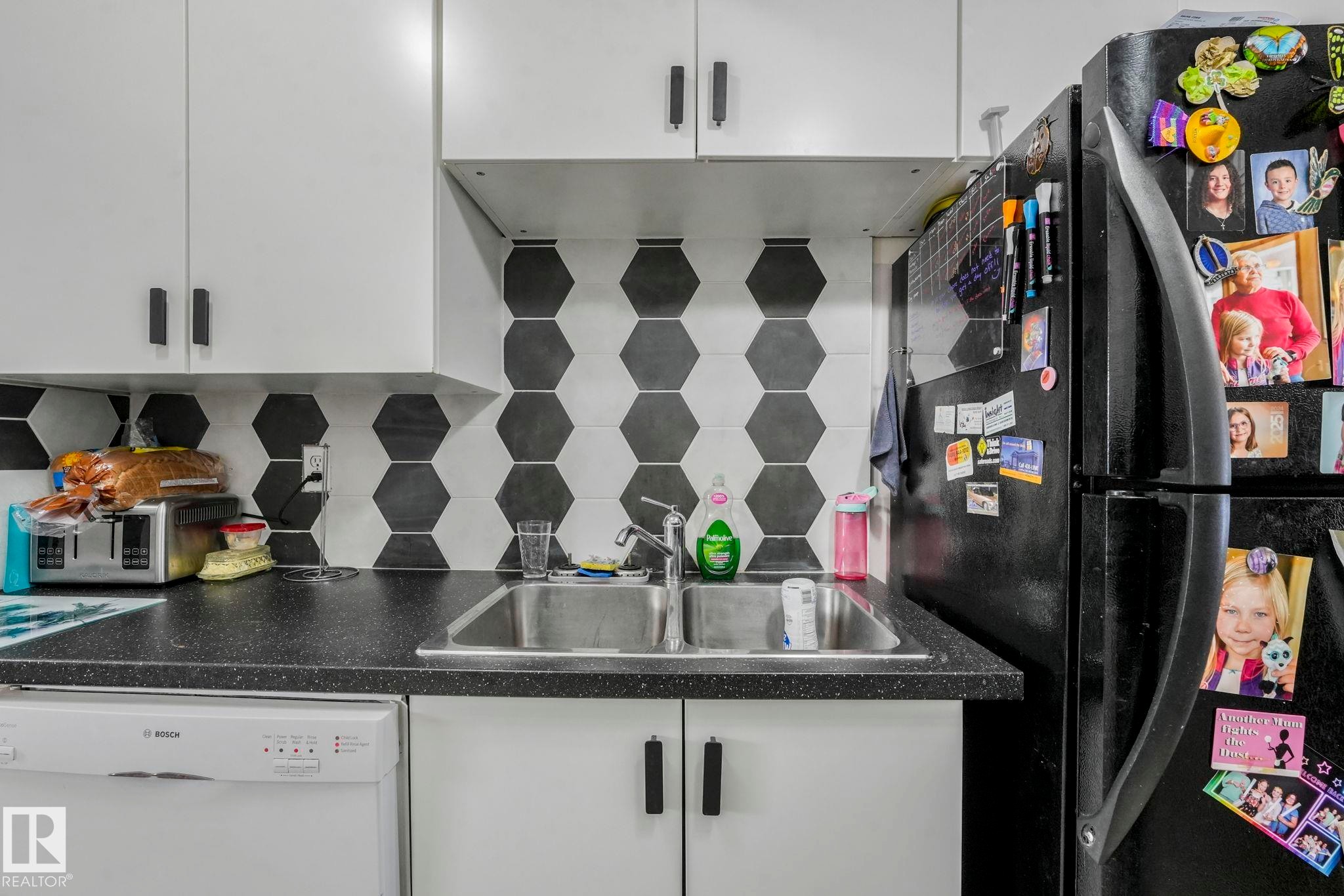 Kitchen featuring white dishwasher, dark countertops, freestanding refrigerator, and white cabinets - 11811 32A Avenue, Edmonton, AB - Indoor Photo Showing Kitchen