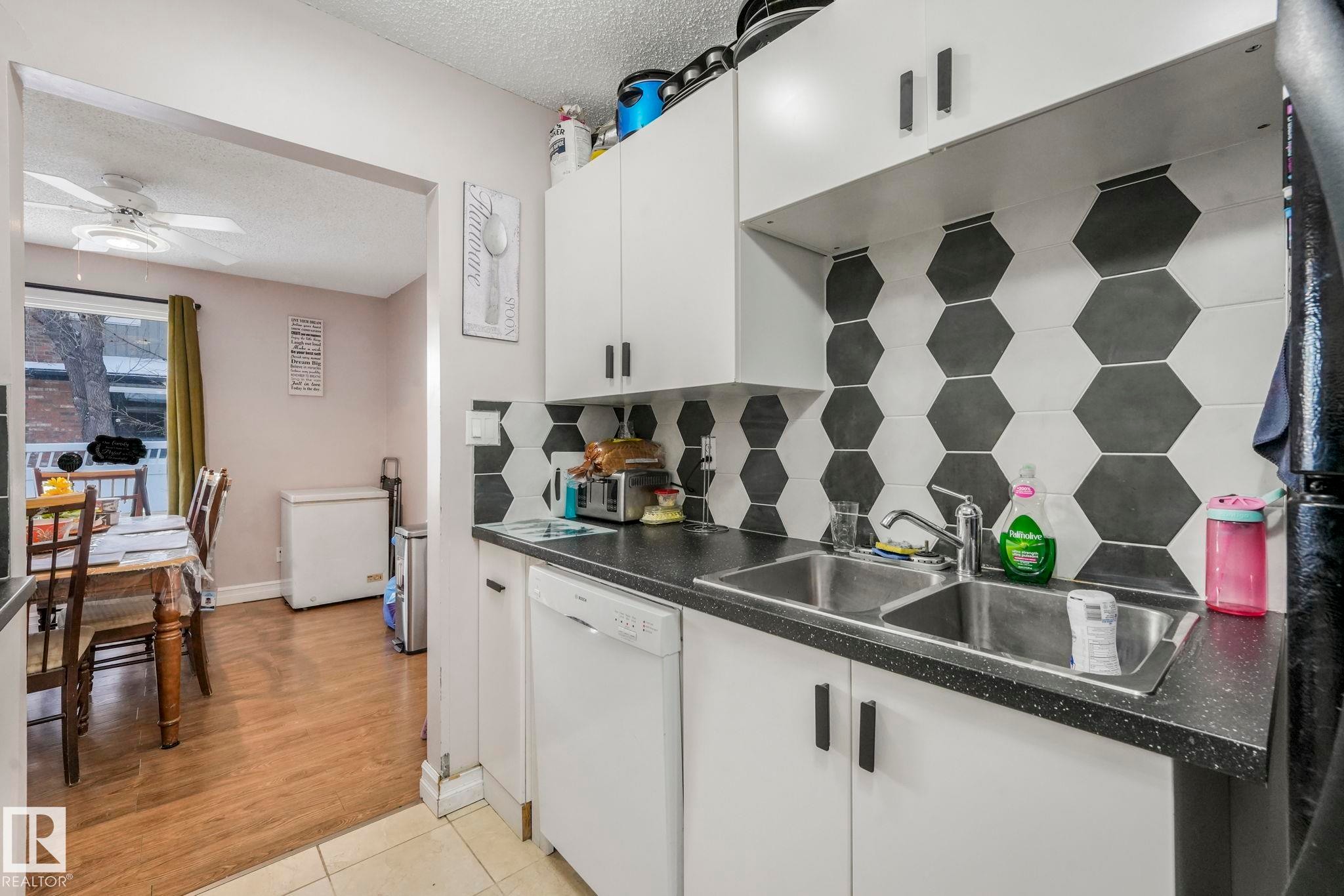 Kitchen with a textured ceiling, white dishwasher, tasteful backsplash, dark countertops, and white cabinets - 11811 32A Avenue, Edmonton, AB - Indoor Photo Showing Kitchen With Double Sink