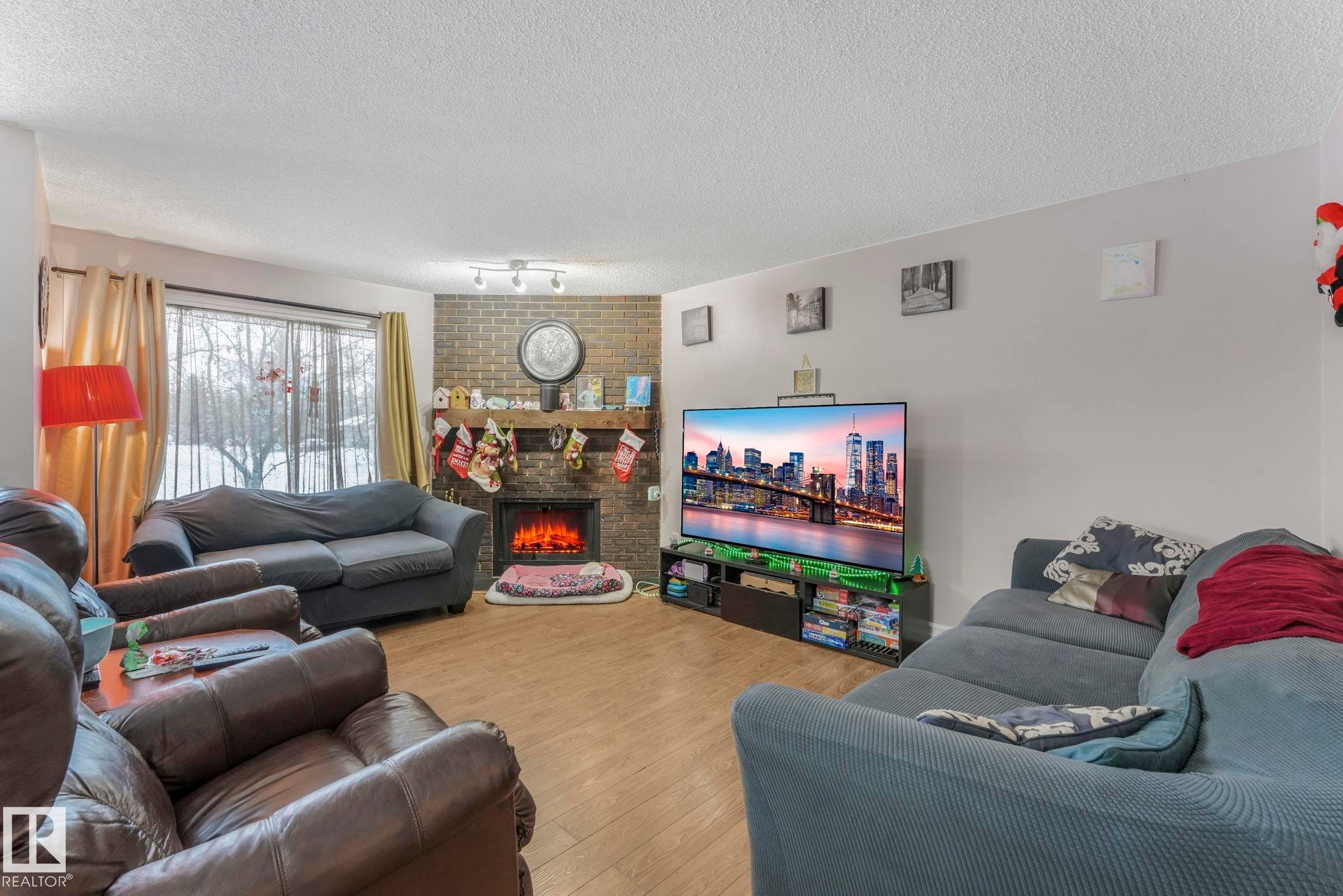 Living area featuring wood finished floors, a fireplace, and a textured ceiling - 11811 32A Avenue, Edmonton, AB - Indoor Photo Showing Living Room