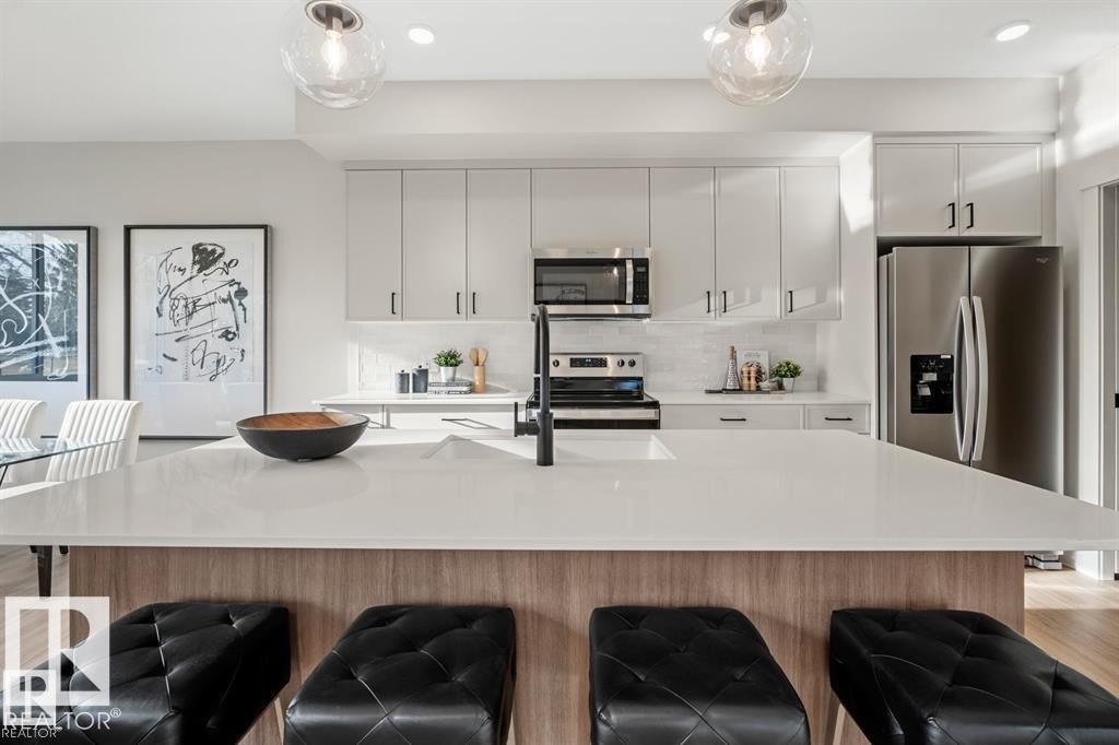 Kitchen featuring stainless steel appliances, light wood finished floors, a kitchen island with sink, decorative backsplash, and a kitchen bar - 24 Grayson Green, Stony Plain, AB - Indoor Photo Showing Kitchen With Upgraded Kitchen