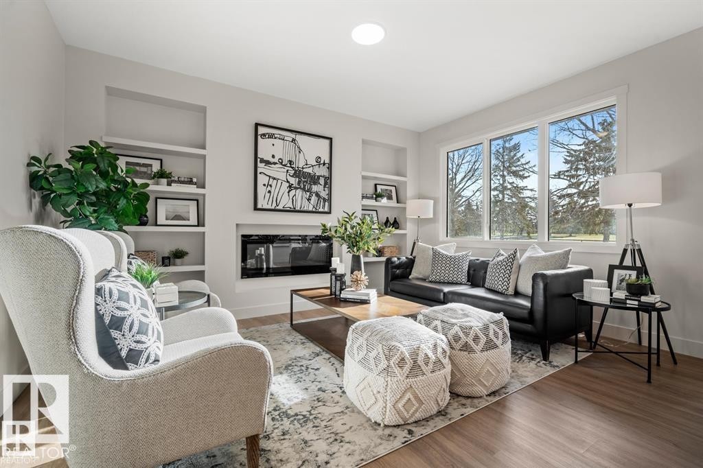 Living area featuring built in shelves, wood finished floors, and a glass covered fireplace - 24 Grayson Green, Stony Plain, AB - Indoor Photo Showing Living Room With Fireplace