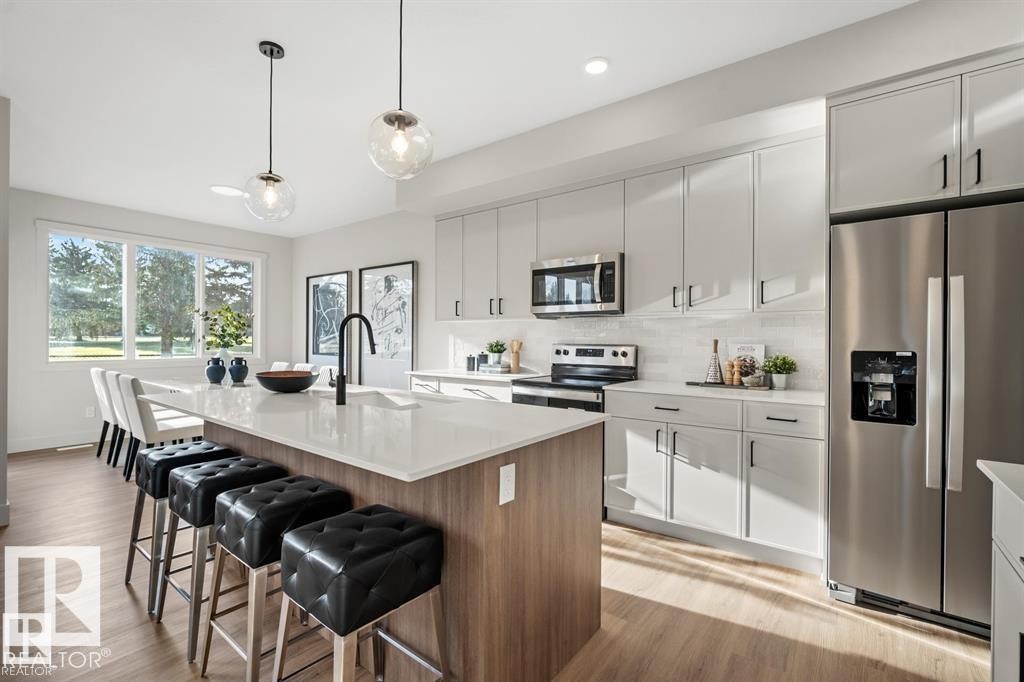 Kitchen with appliances with stainless steel finishes, pendant lighting, an island with sink, a kitchen breakfast bar, and light wood finished floors - 24 Grayson Green, Stony Plain, AB - Indoor Photo Showing Kitchen With Upgraded Kitchen