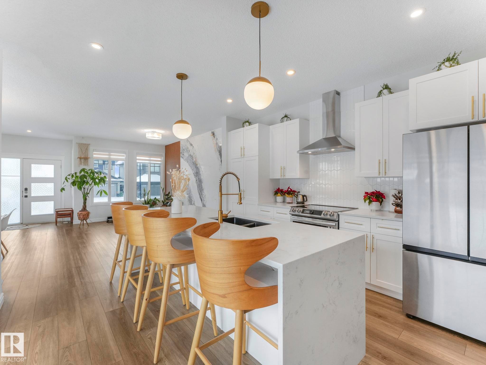 Kitchen featuring stainless steel appliances, wall chimney exhaust hood, a kitchen breakfast bar, hanging light fixtures, and white cabinets - 4447 Kinsella Green, Edmonton, AB - Indoor Photo Showing Kitchen With Double Sink With Upgraded Kitchen