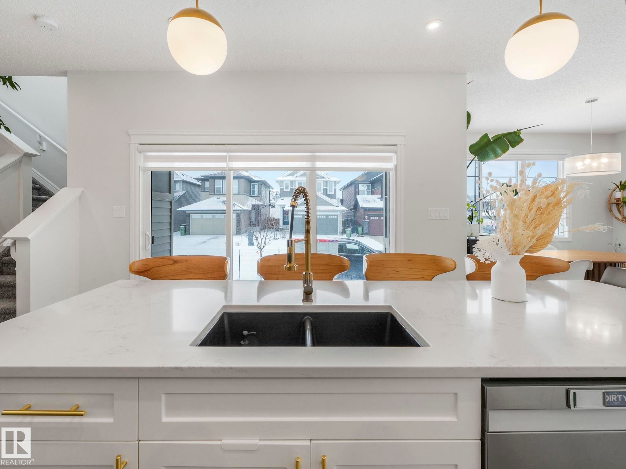 Kitchen with white cabinetry, light stone countertops, decorative light fixtures, dishwasher, and healthy amount of natural light - 4447 Kinsella Green, Edmonton, AB - Indoor Photo Showing Kitchen