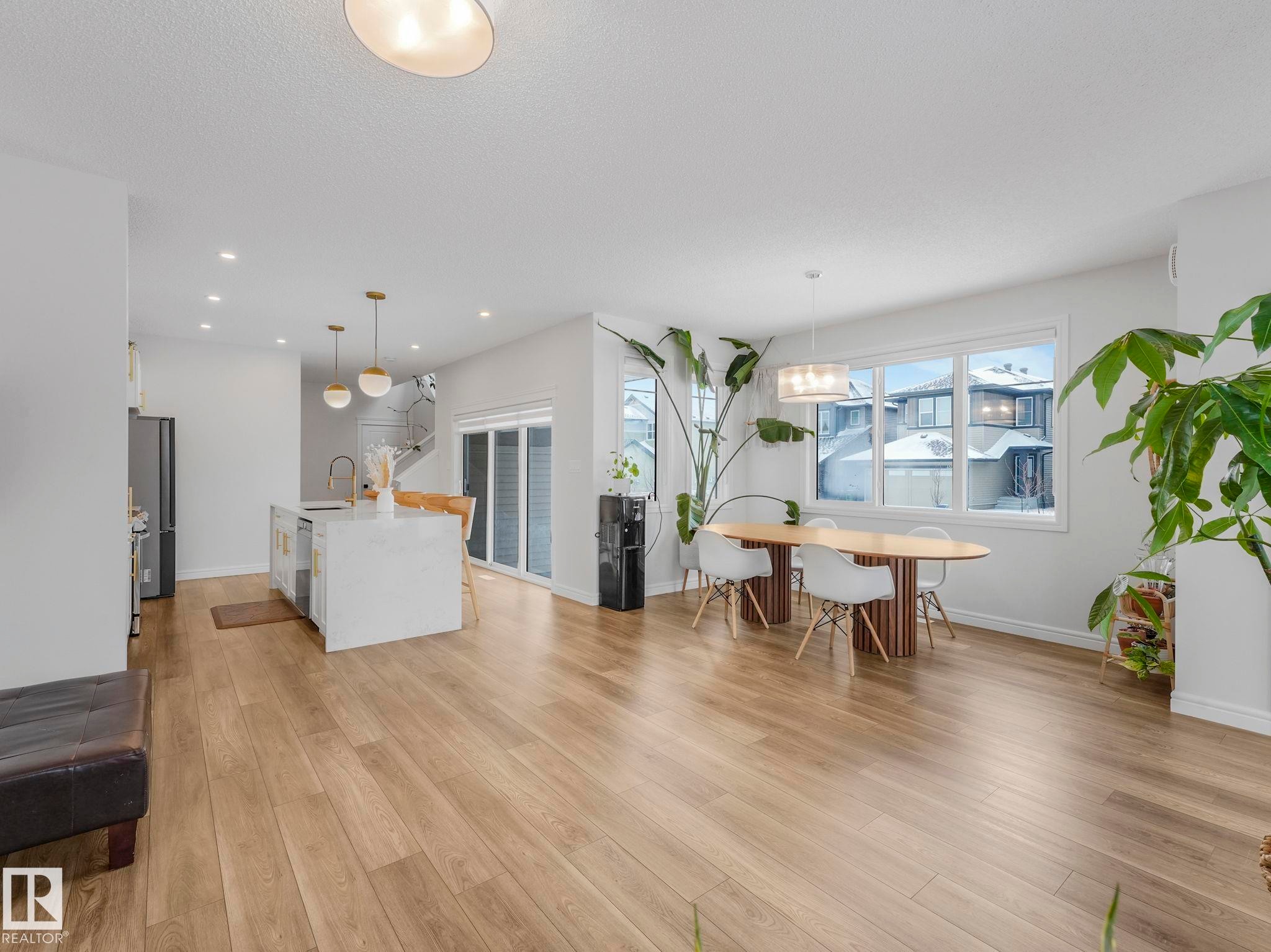 Kitchen with a center island with sink, light stone countertops, hanging light fixtures, light wood-style floors, and recessed lighting - 4447 Kinsella Green, Edmonton, AB - Indoor