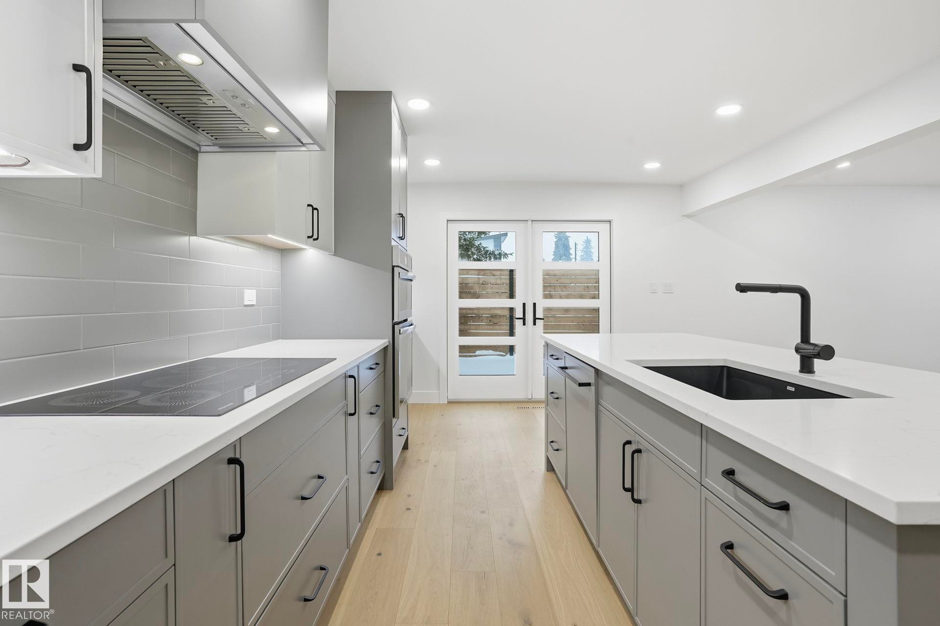 Kitchen with gray cabinetry, extractor fan, light wood-style floors, light stone counters, and black electric cooktop - 14604 Mackenzie Drive, Edmonton, AB - Indoor Photo Showing Kitchen With Upgraded Kitchen