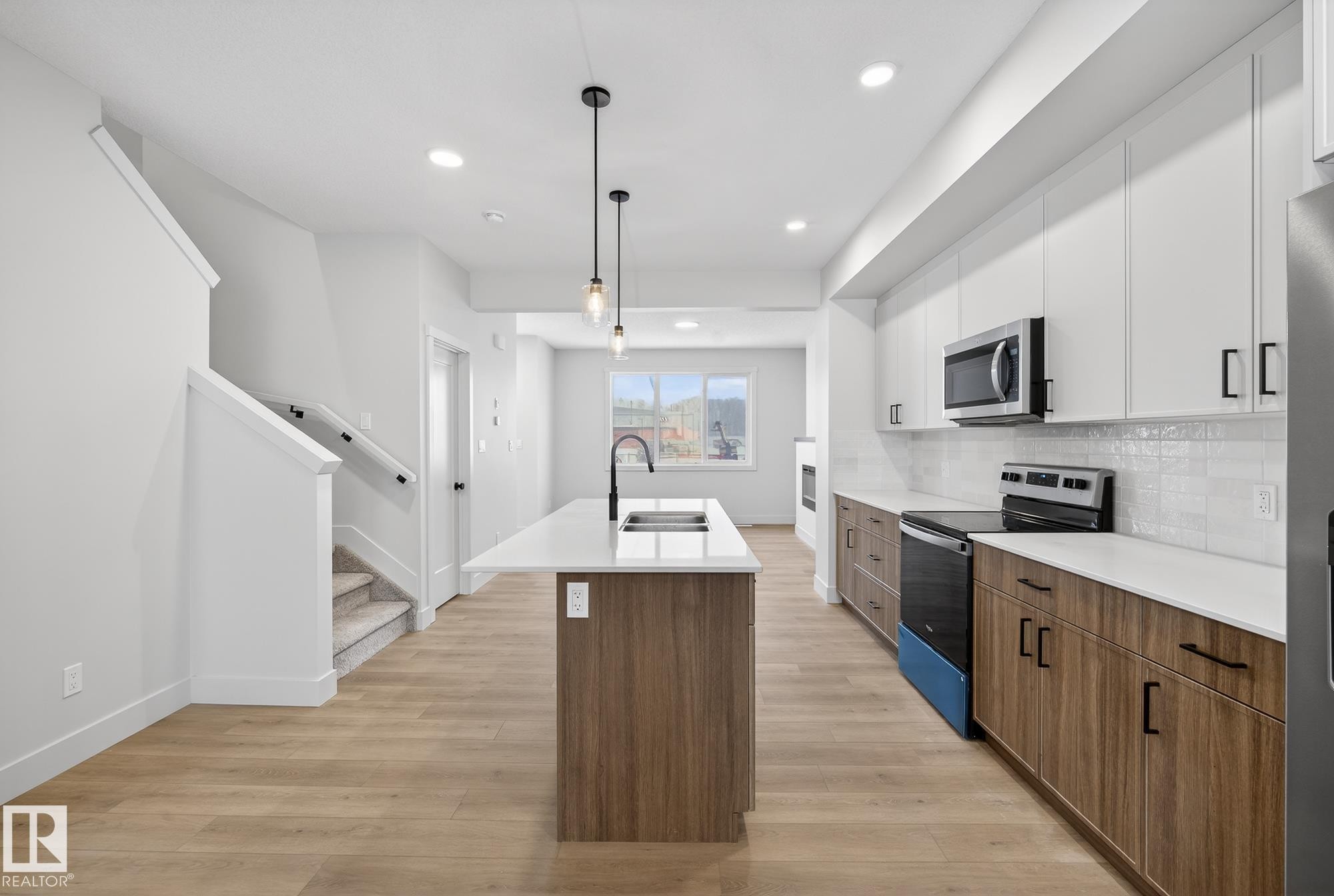 Kitchen featuring brown cabinetry, range with electric cooktop, a kitchen island with sink, modern cabinets, and light wood-style floors - 119 Brickyard Drive, Stony Plain, AB - Indoor Photo Showing Kitchen With Double Sink With Upgraded Kitchen