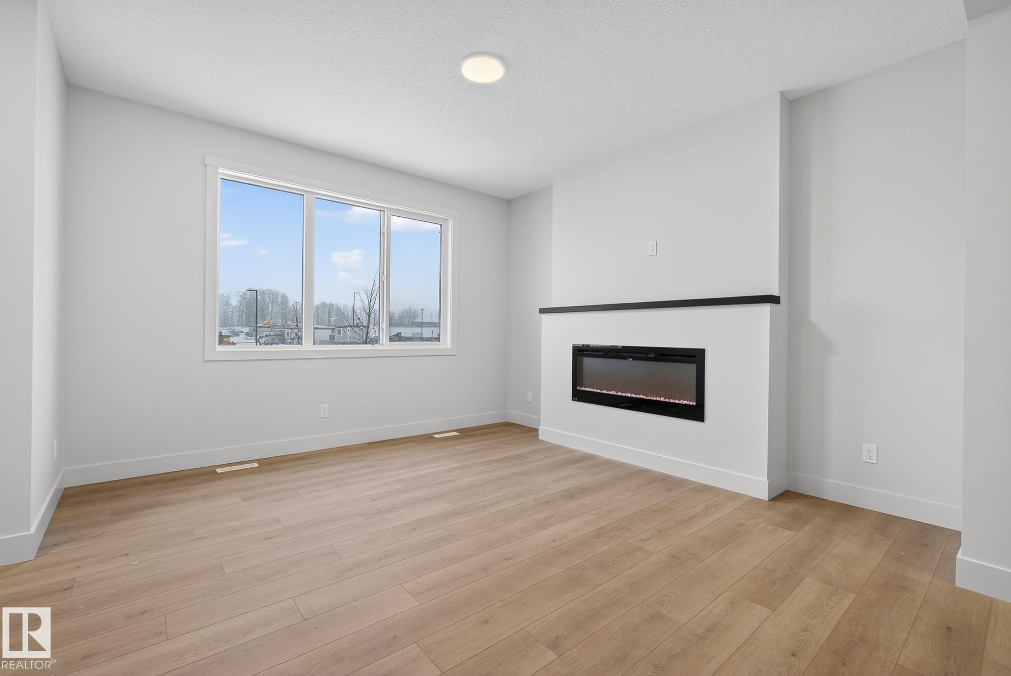 Unfurnished living room with light wood finished floors, a glass covered fireplace, and a textured ceiling - 119 Brickyard Drive, Stony Plain, AB - Indoor Photo Showing Living Room With Fireplace