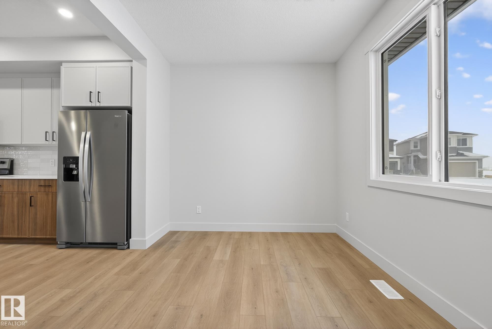 Kitchen with stainless steel refrigerator with ice dispenser, white cabinets, backsplash, light wood-type flooring, and light countertops - 119 Brickyard Drive, Stony Plain, AB - Indoor