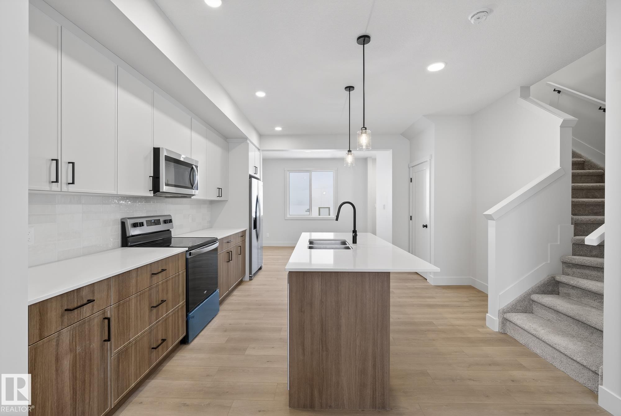 Kitchen featuring brown cabinetry, stainless steel appliances, white cabinetry, modern cabinets, and an island with sink - 119 Brickyard Drive, Stony Plain, AB - Indoor Photo Showing Kitchen With Double Sink With Upgraded Kitchen