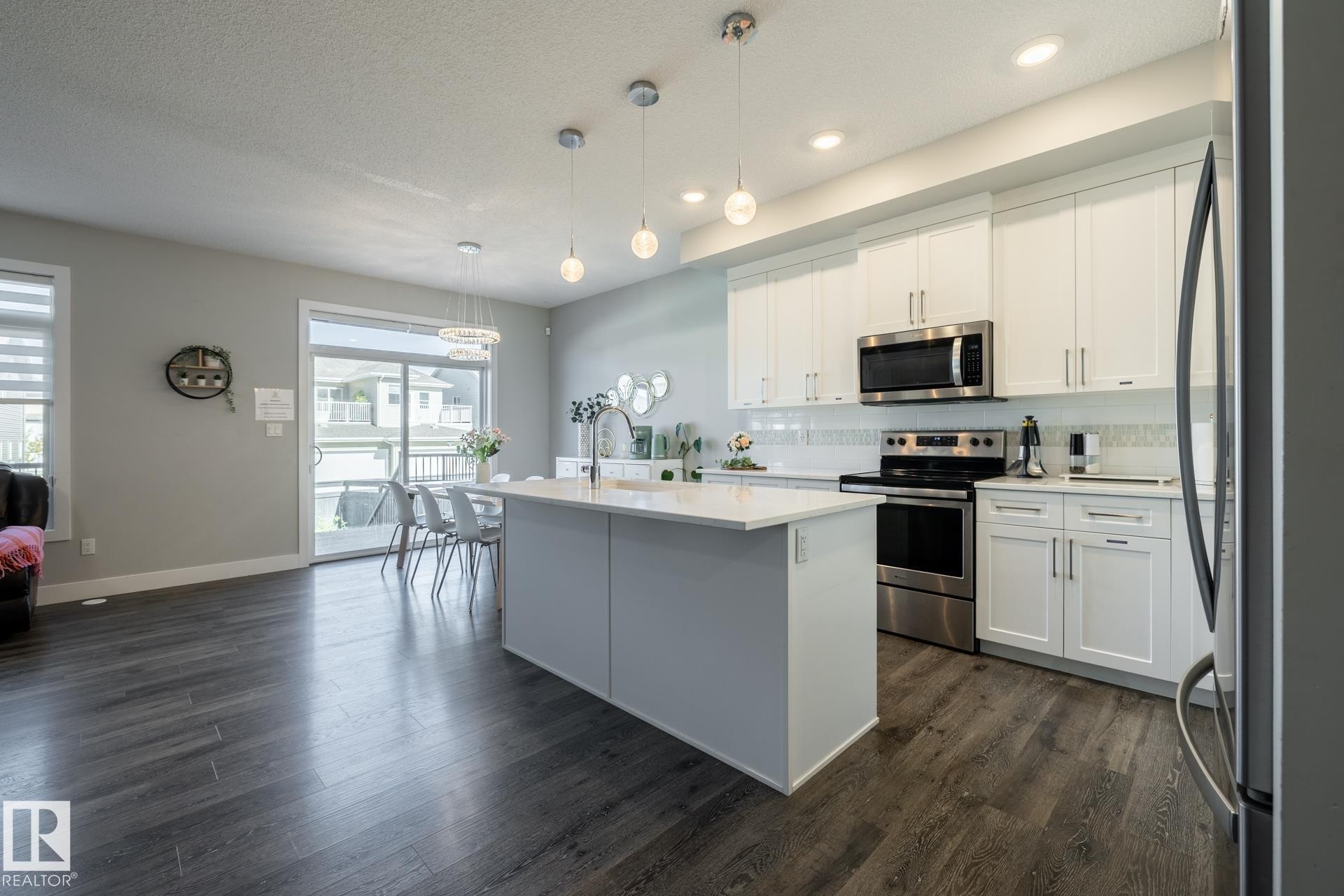 Kitchen featuring appliances with stainless steel finishes, backsplash, white cabinetry, a kitchen island with sink, and a textured ceiling - 1440 Darby Green, Edmonton, AB - Indoor Photo Showing Kitchen With Upgraded Kitchen