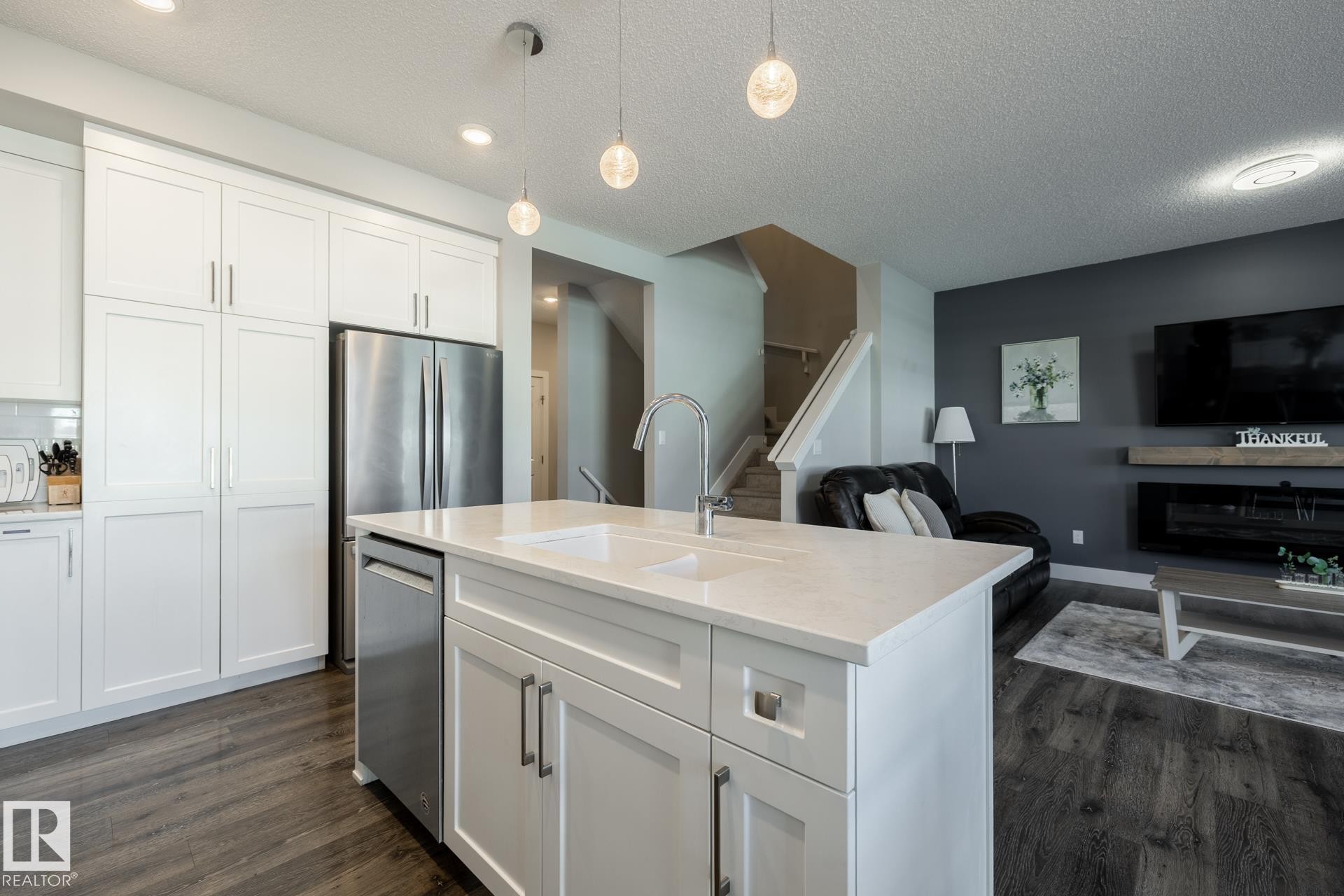 Kitchen featuring white cabinetry, open floor plan, dark wood-style flooring, a textured ceiling, and pendant lighting - 1440 Darby Green, Edmonton, AB - Indoor Photo Showing Kitchen With Double Sink
