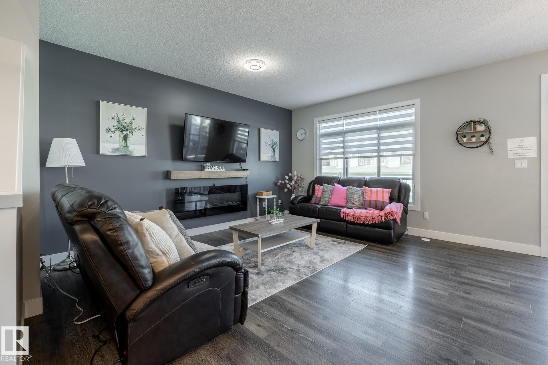 Living room with wood finished floors, a textured ceiling, and a glass covered fireplace - 1440 Darby Green, Edmonton, AB - Indoor Photo Showing Living Room With Fireplace