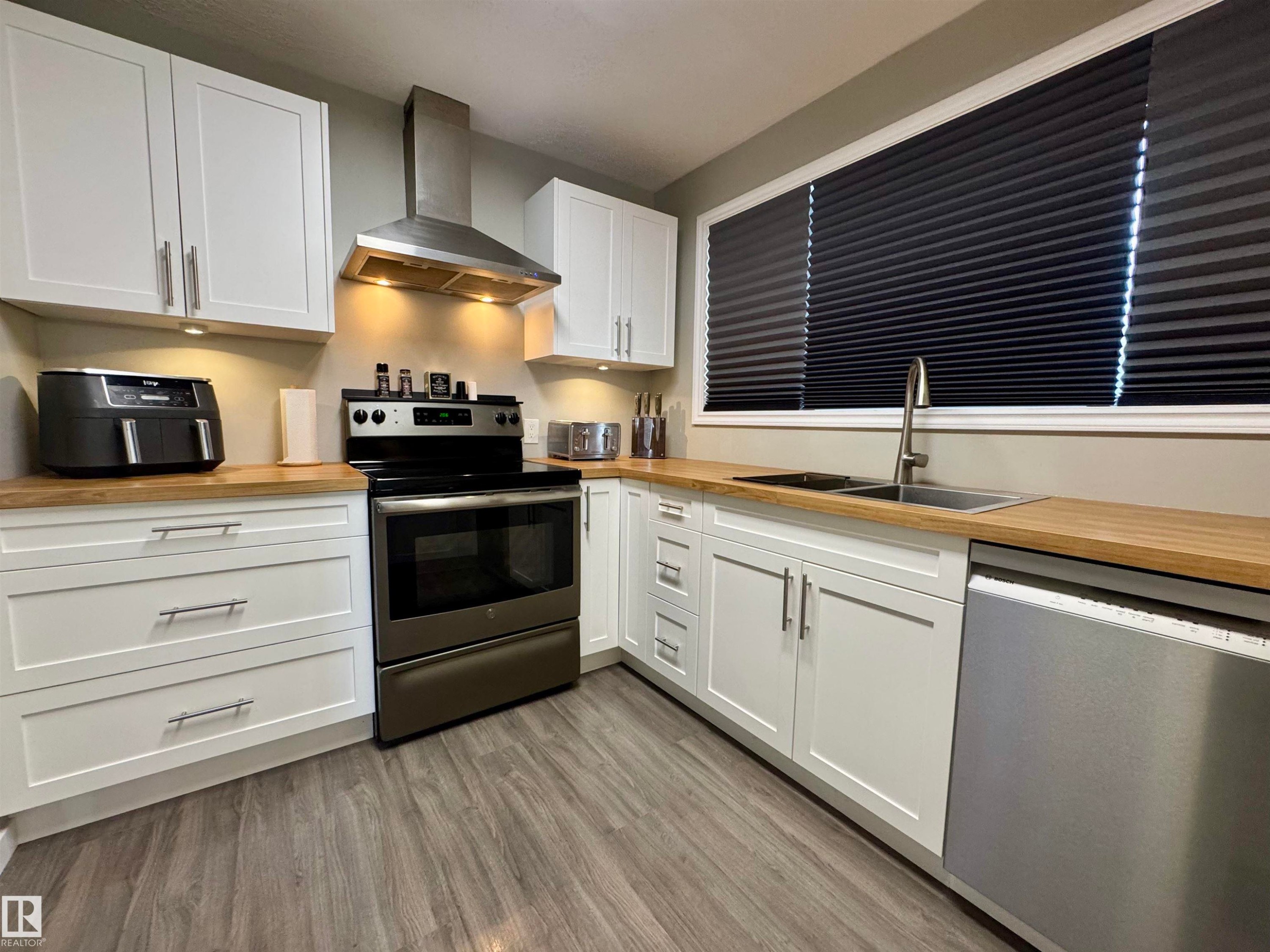 Kitchen featuring appliances with stainless steel finishes, wall chimney exhaust hood, white cabinets, and light wood finished floors - 5140 52 Avenue, Ryley, AB - Indoor Photo Showing Kitchen With Double Sink