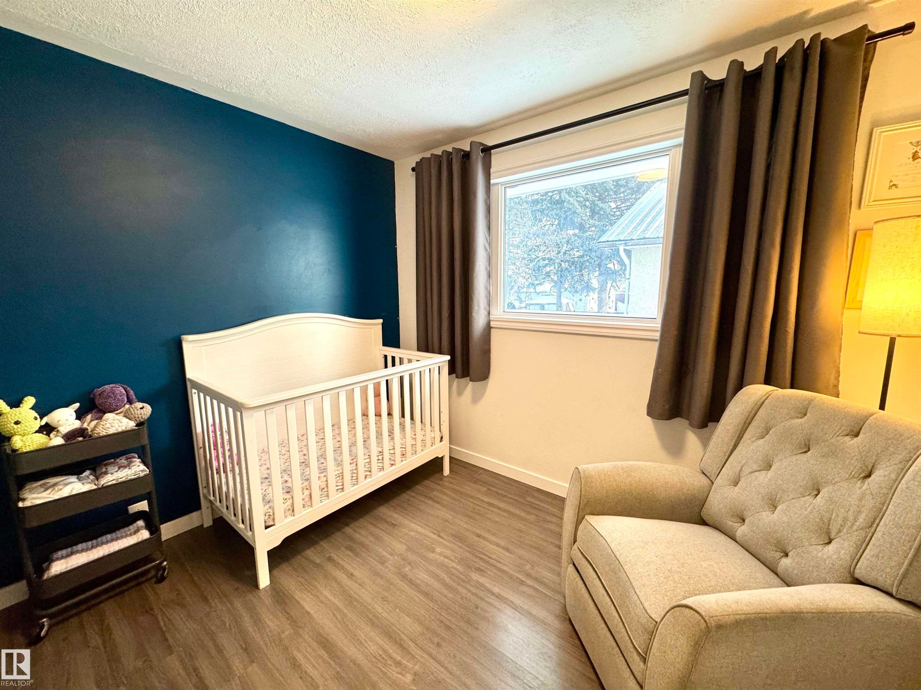 Bedroom featuring a textured ceiling, a crib, and wood finished floors - 5140 52 Avenue, Ryley, AB - Indoor Photo Showing Bedroom