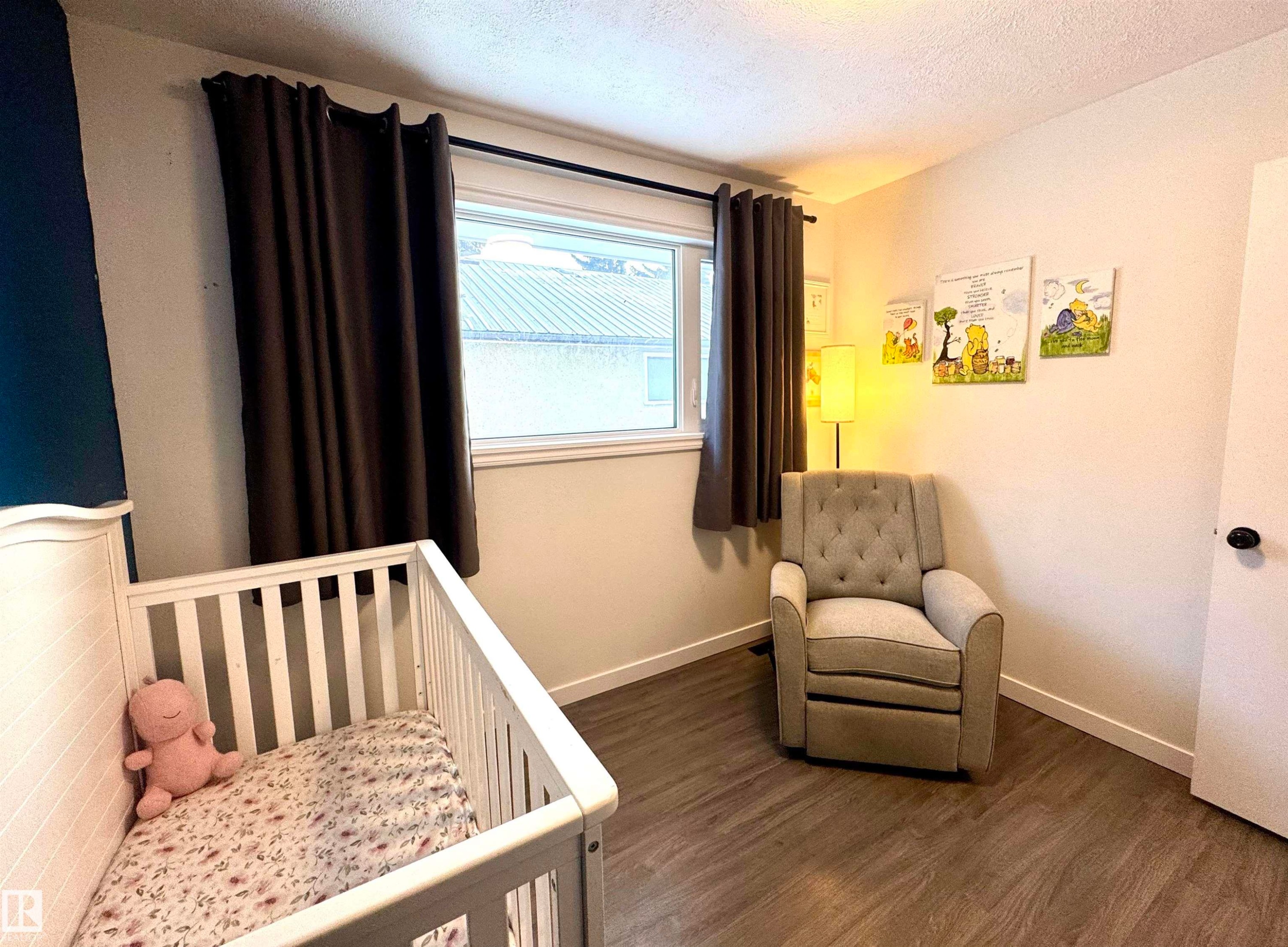 Bedroom featuring a textured ceiling, dark wood-type flooring, and a crib - 5140 52 Avenue, Ryley, AB - Indoor