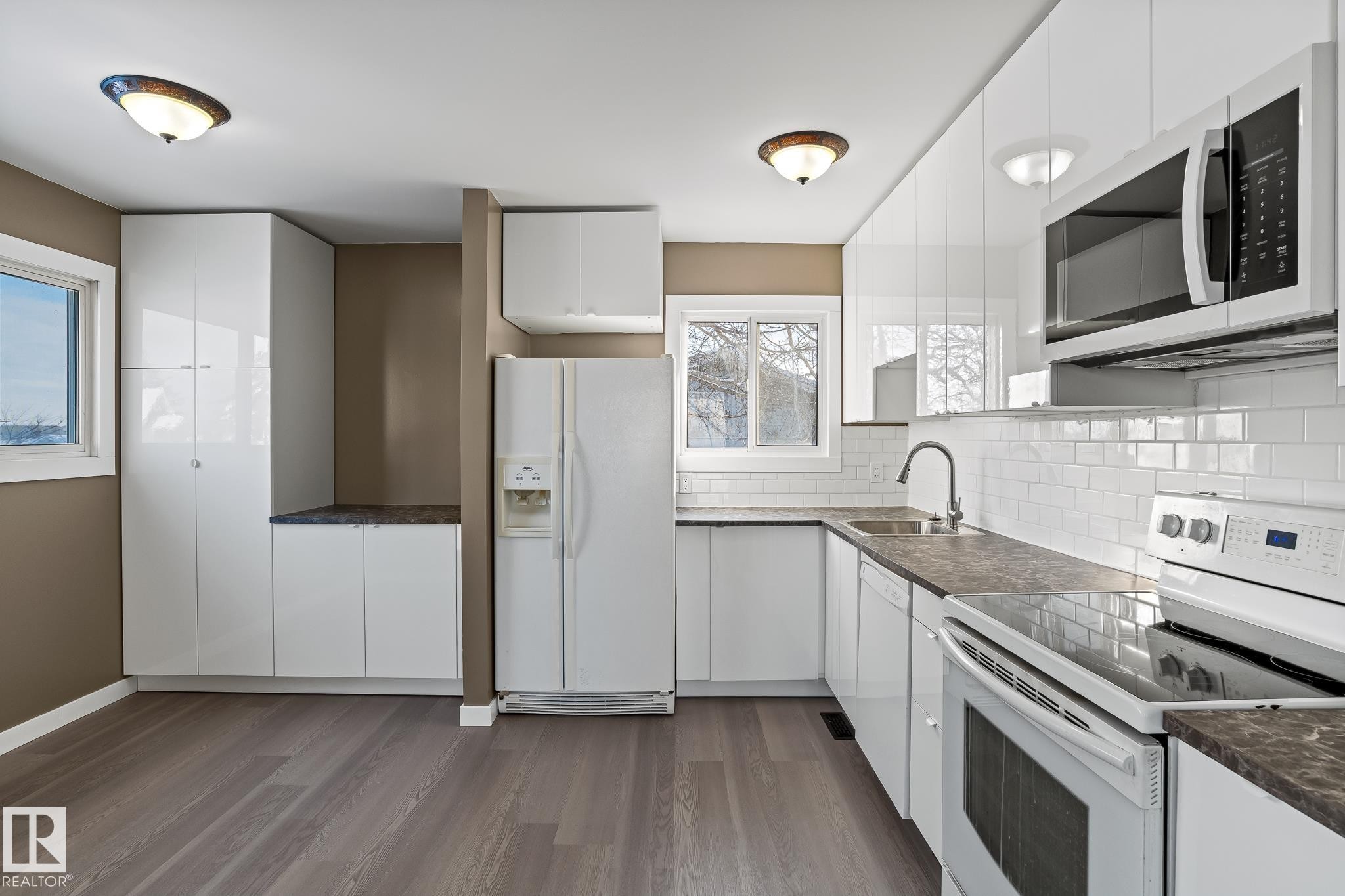 Kitchen featuring white appliances, white cabinets, dark countertops, and dark wood-style flooring - 315 10 Street, Cold Lake, AB - Indoor Photo Showing Kitchen With Upgraded Kitchen