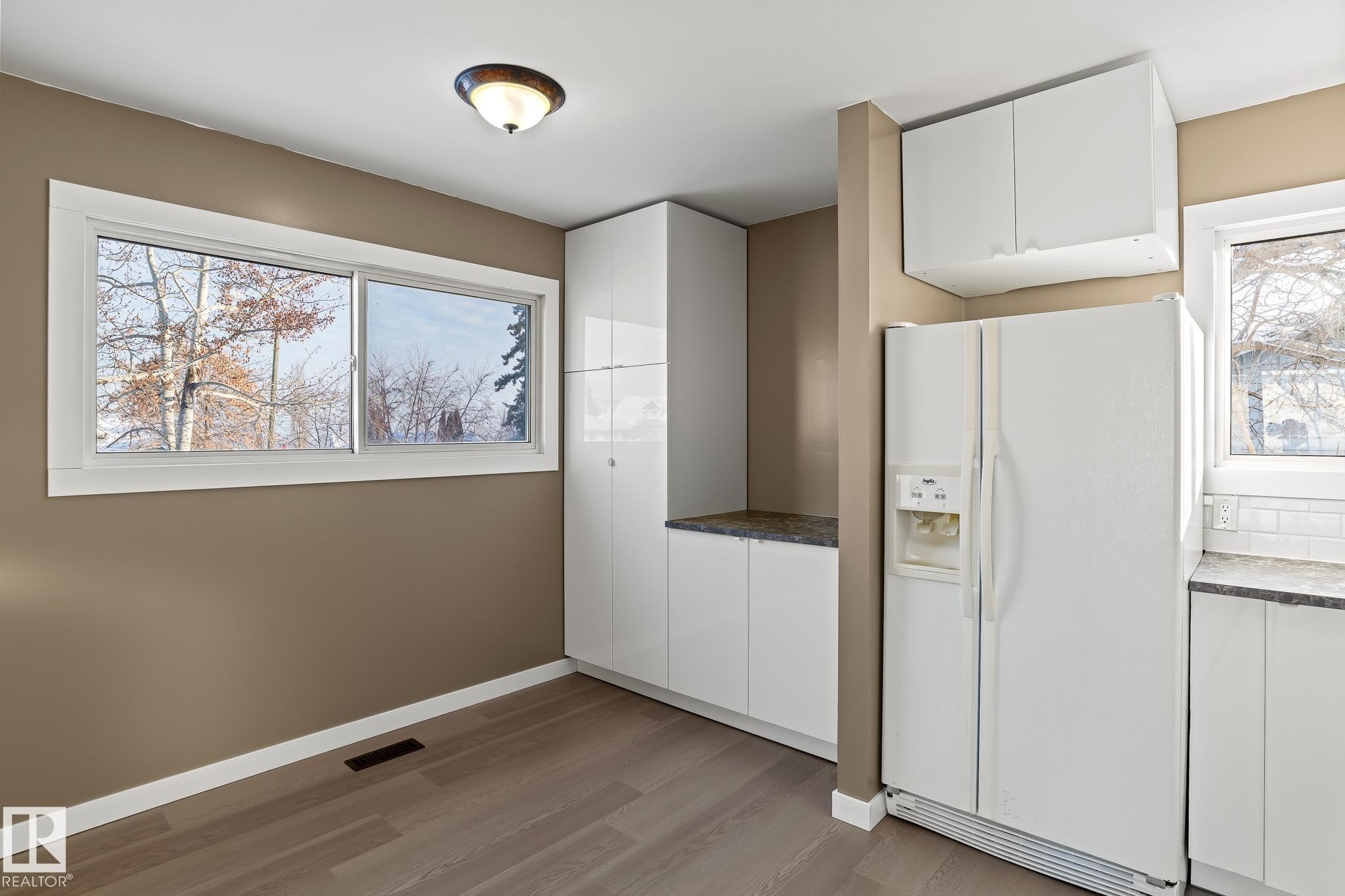 Kitchen featuring white refrigerator with ice dispenser, white cabinetry, light wood finished floors, and dark stone countertops - 315 10 Street, Cold Lake, AB - Indoor Photo Showing Other Room