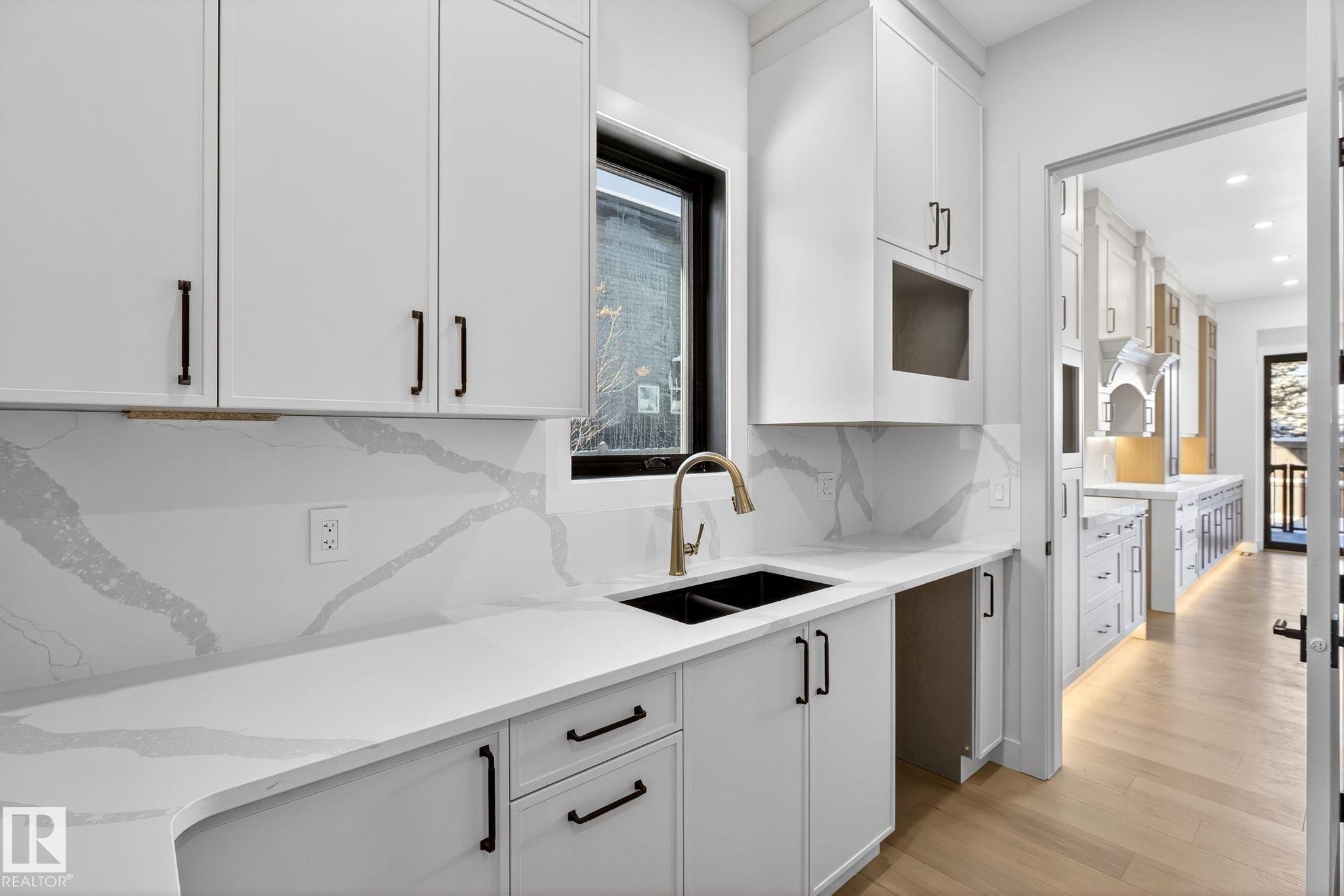 Kitchen featuring white cabinetry, light wood-type flooring, tasteful backsplash, and light stone counters - 1926 Ainslie Link, Edmonton, AB - Indoor Photo Showing Kitchen With Double Sink