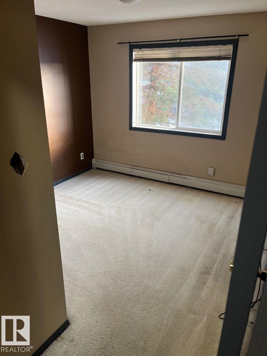 Unfurnished room featuring light carpet, baseboard heating, and a textured ceiling - 231 1180 Hyndman Road, Edmonton, AB - Indoor Photo Showing Other Room