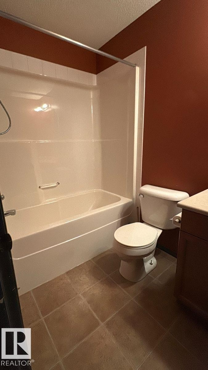 Full bath featuring vanity, tub / shower combination, dark tile patterned floors, and a textured ceiling - 231 1180 Hyndman Road, Edmonton, AB - Indoor Photo Showing Bathroom