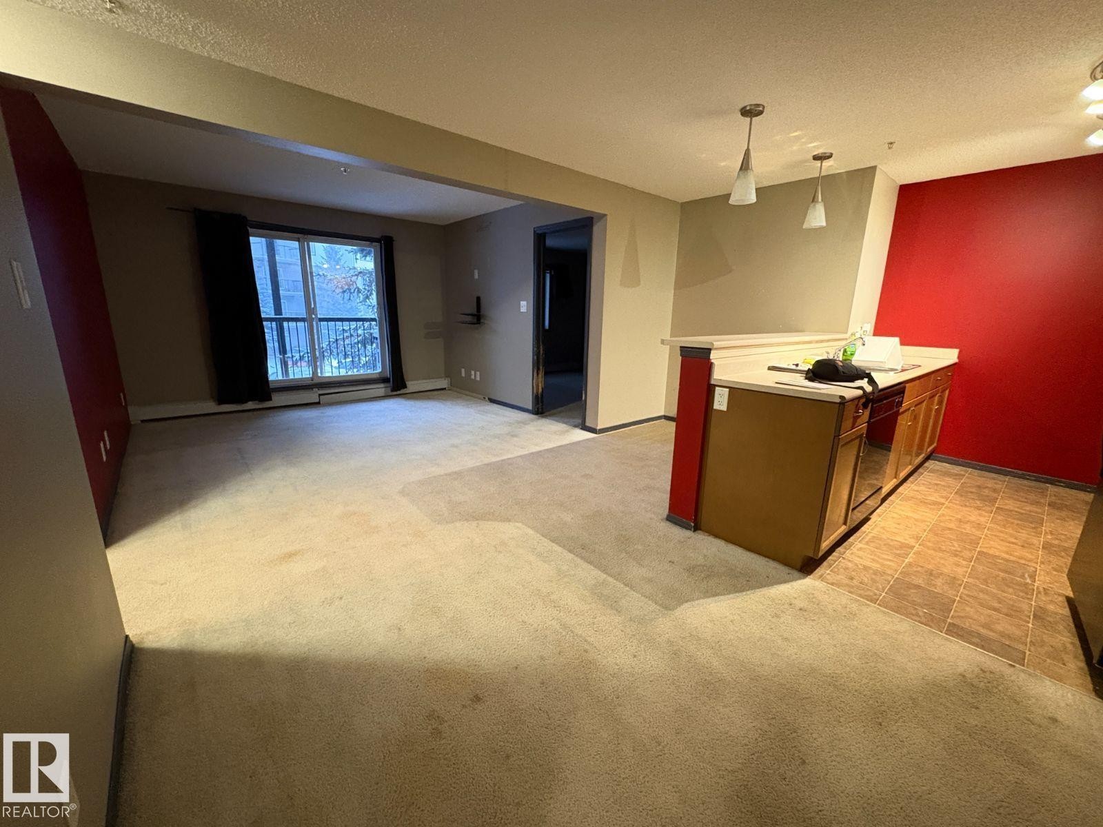 Kitchen with light countertops, light carpet, a peninsula, decorative light fixtures, and open floor plan - 231 1180 Hyndman Road, Edmonton, AB - Indoor