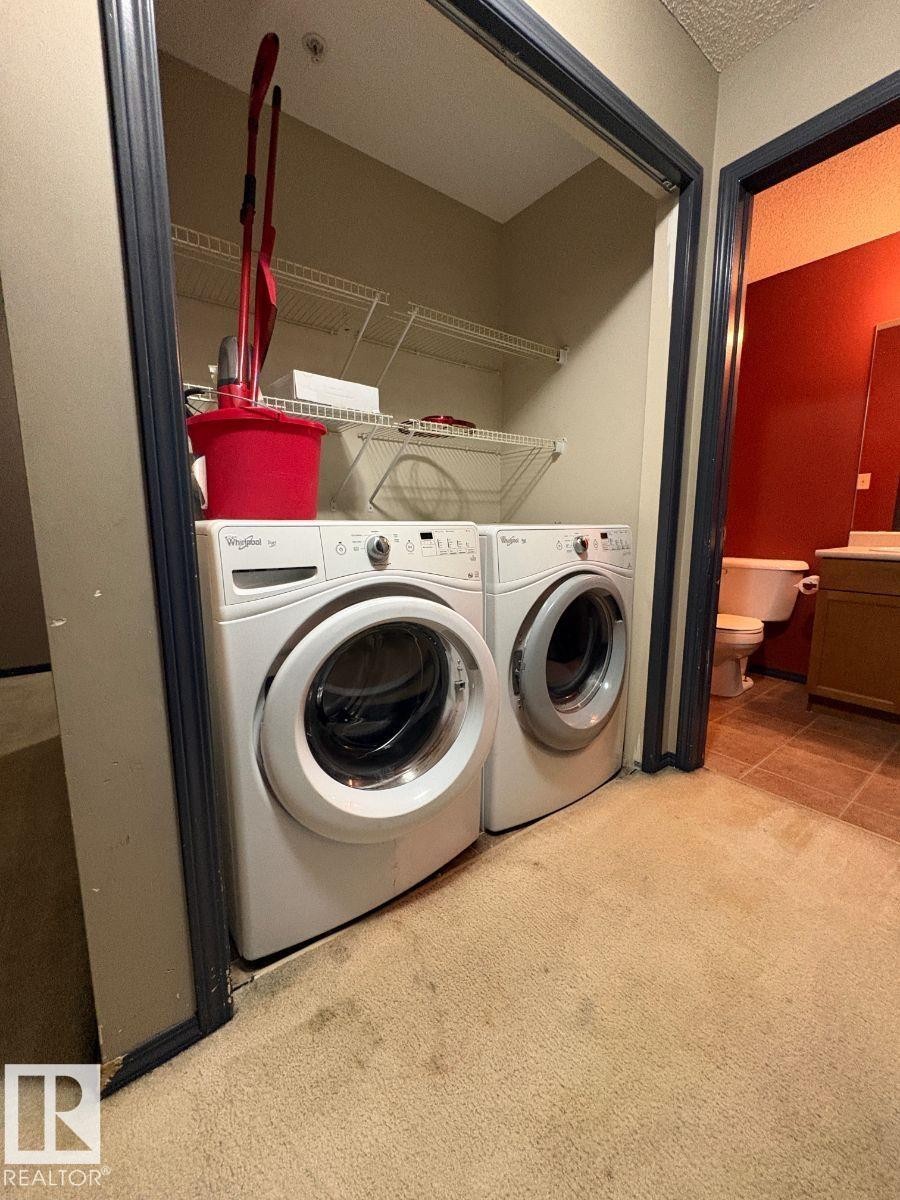 Laundry area with washing machine and dryer, a textured ceiling, and light colored carpet - 231 1180 Hyndman Road, Edmonton, AB - Indoor Photo Showing Laundry Room