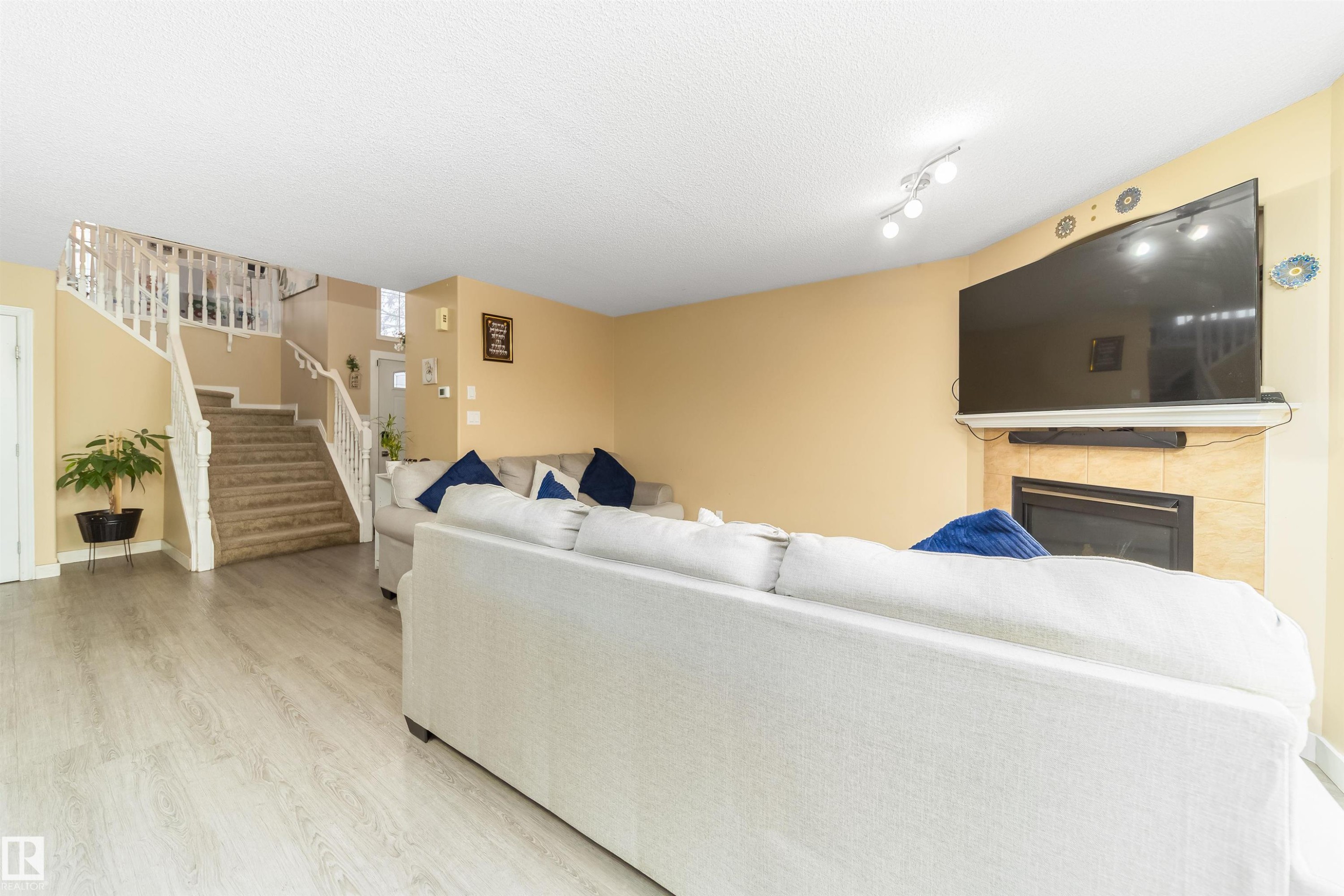 Living area featuring a fireplace, stairway, light wood finished floors, and a textured ceiling - 8518 6 Av, Edmonton, AB - Indoor