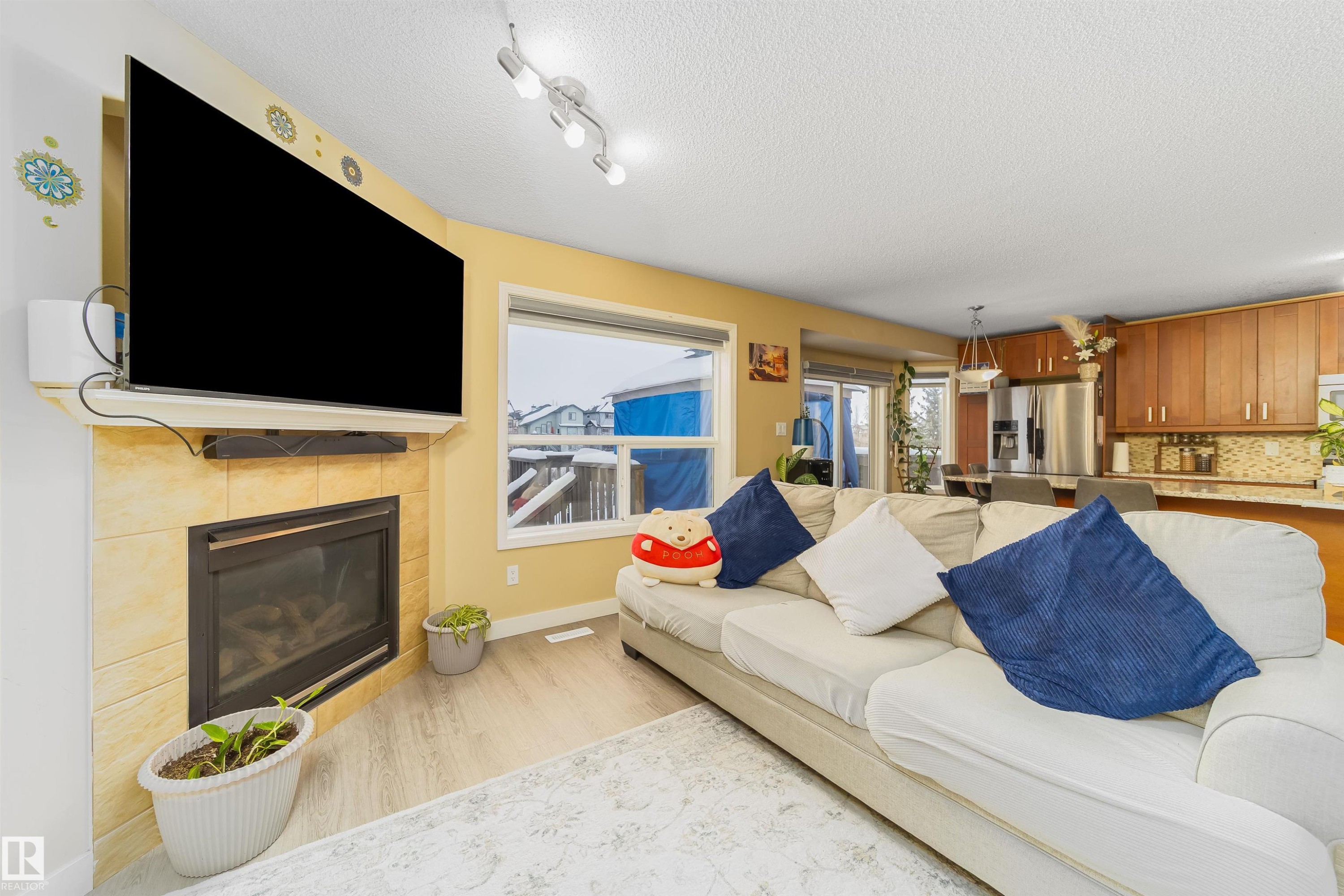 Living room featuring a textured ceiling, light wood-type flooring, and a tiled fireplace - 8518 6 Av, Edmonton, AB - Indoor Photo Showing Living Room With Fireplace