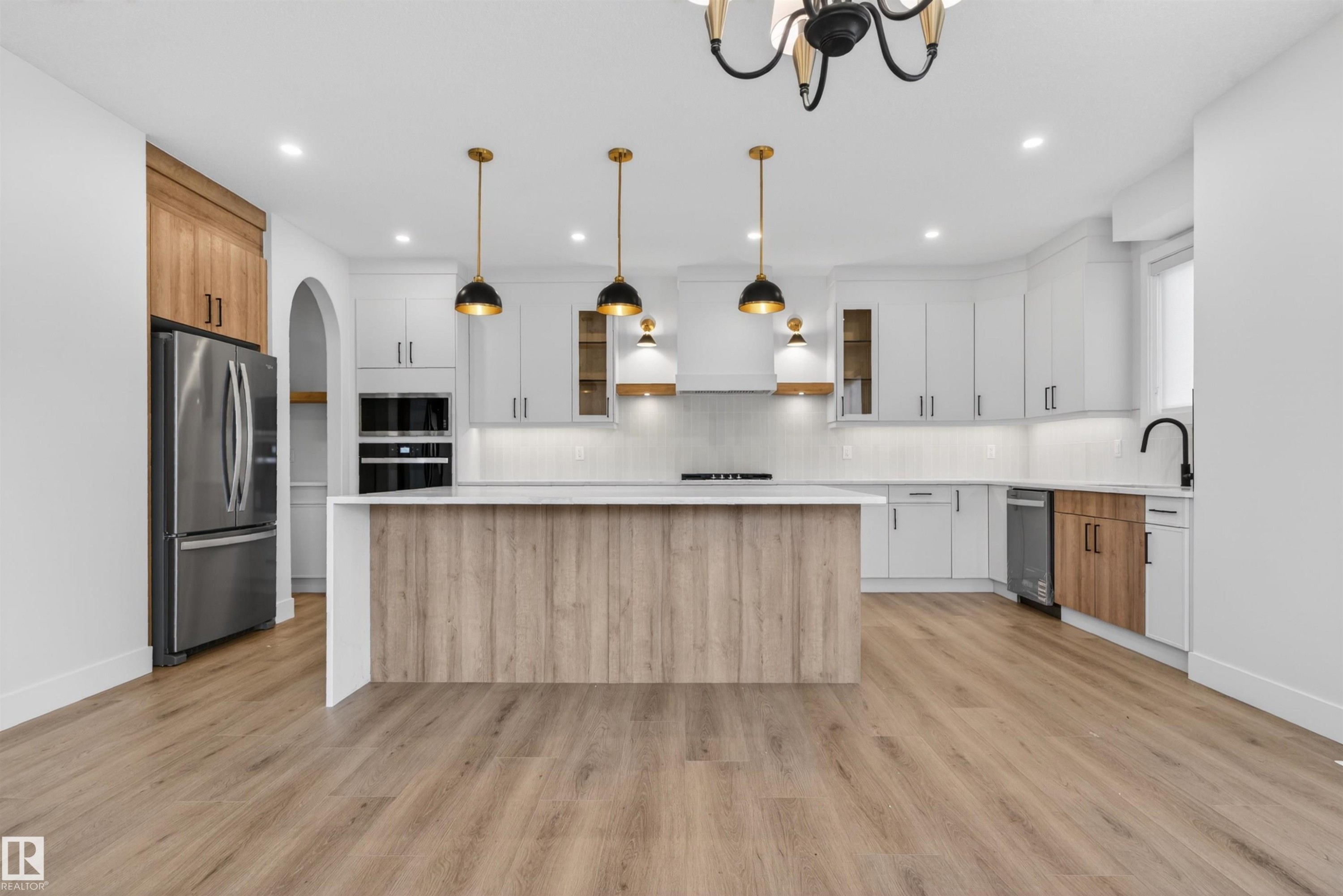 Kitchen featuring a central island with wood-finish paneling, white countertops, stainless steel appliances, white cabinetry, and wood-finish flooring - 27 Redpoll Wynd, St. Albert, AB - Indoor Photo Showing Kitchen With Upgraded Kitchen