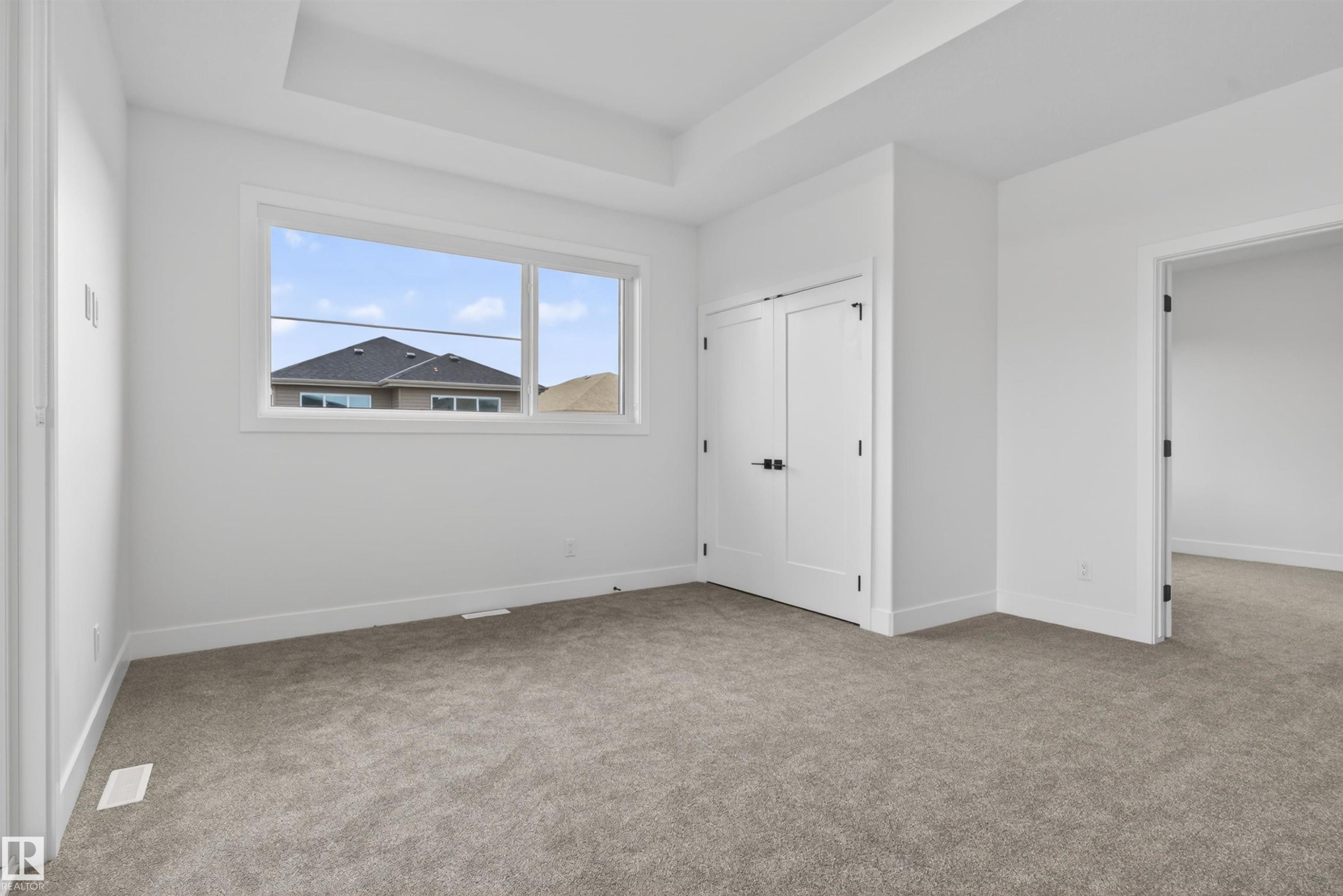 Bright room featuring a large window, tray ceiling, plush carpeting, and contemporary doors with dark hardware - 27 Redpoll Wynd, St. Albert, AB - Indoor Photo Showing Other Room