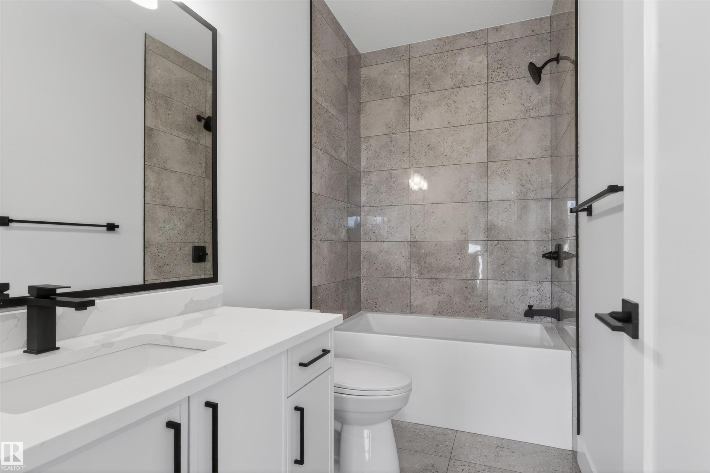 Bathroom featuring a white vanity with integrated sink, matte black fixtures, a rectangular mirror, a bathtub with a tiled surround, and coordinating floor tiles - 27 Redpoll Wynd, St. Albert, AB - Indoor Photo Showing Bathroom