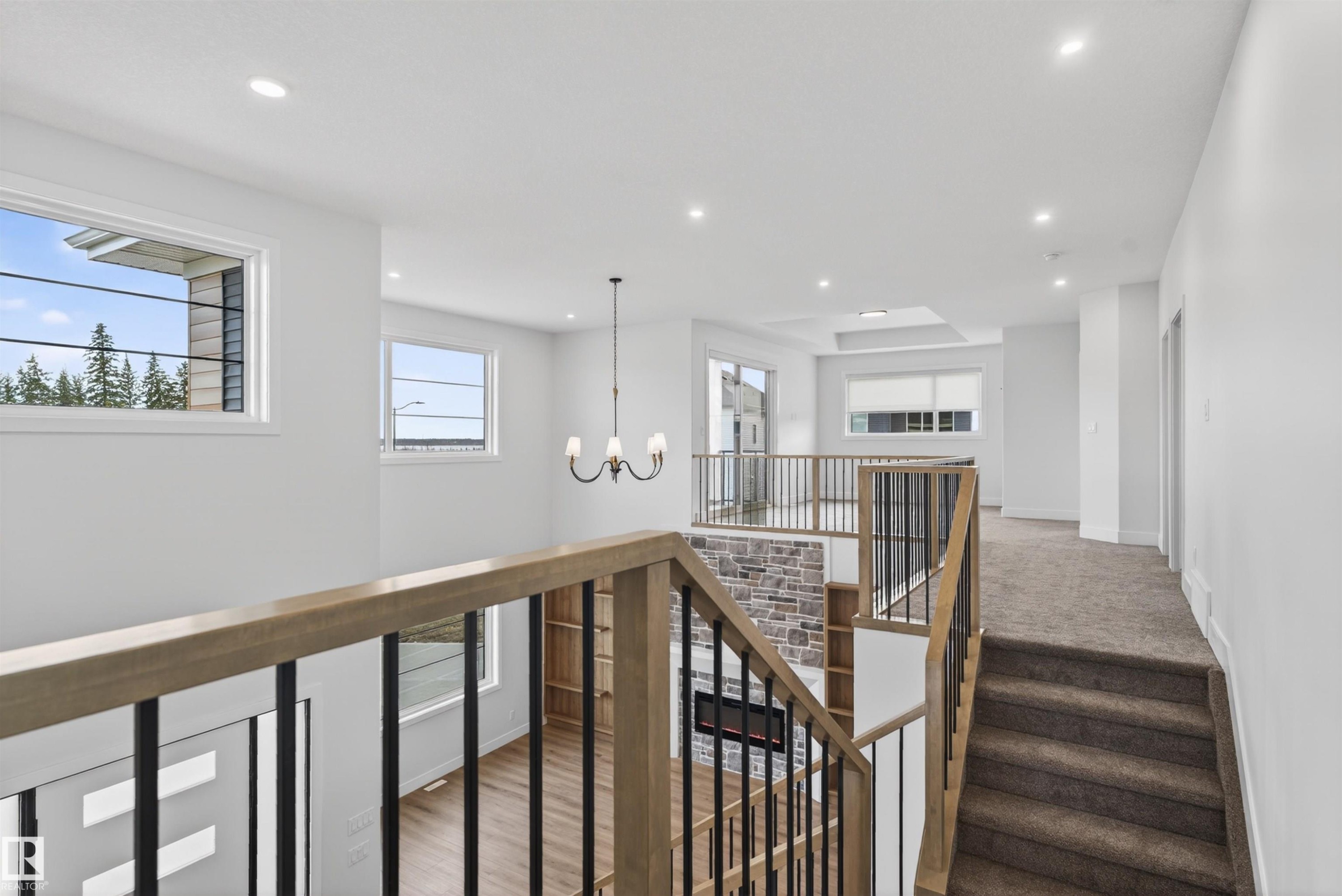 Open upper landing featuring a carpeted hallway and wood-finish handrails with black metal balusters - 27 Redpoll Wynd, St. Albert, AB - Indoor Photo Showing Other Room