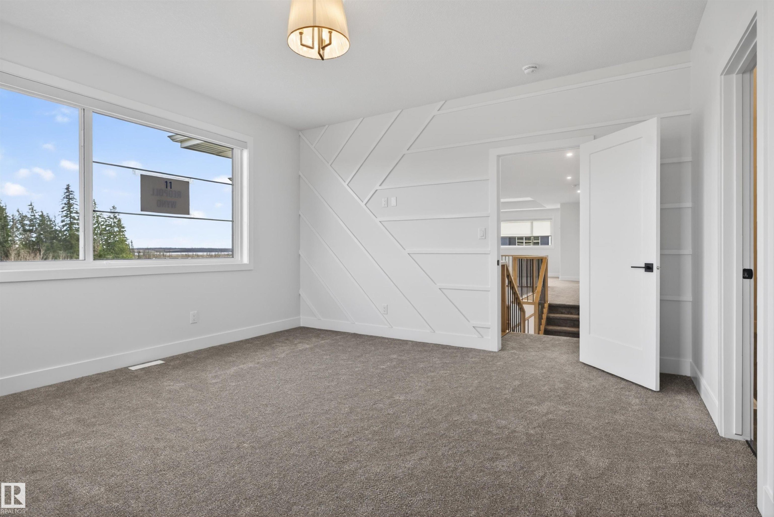 Spacious room featuring a decorative accent wall, large windows, neutral carpeting, and a modern semi-flush mount light fixture - 27 Redpoll Wynd, St. Albert, AB - Indoor Photo Showing Other Room