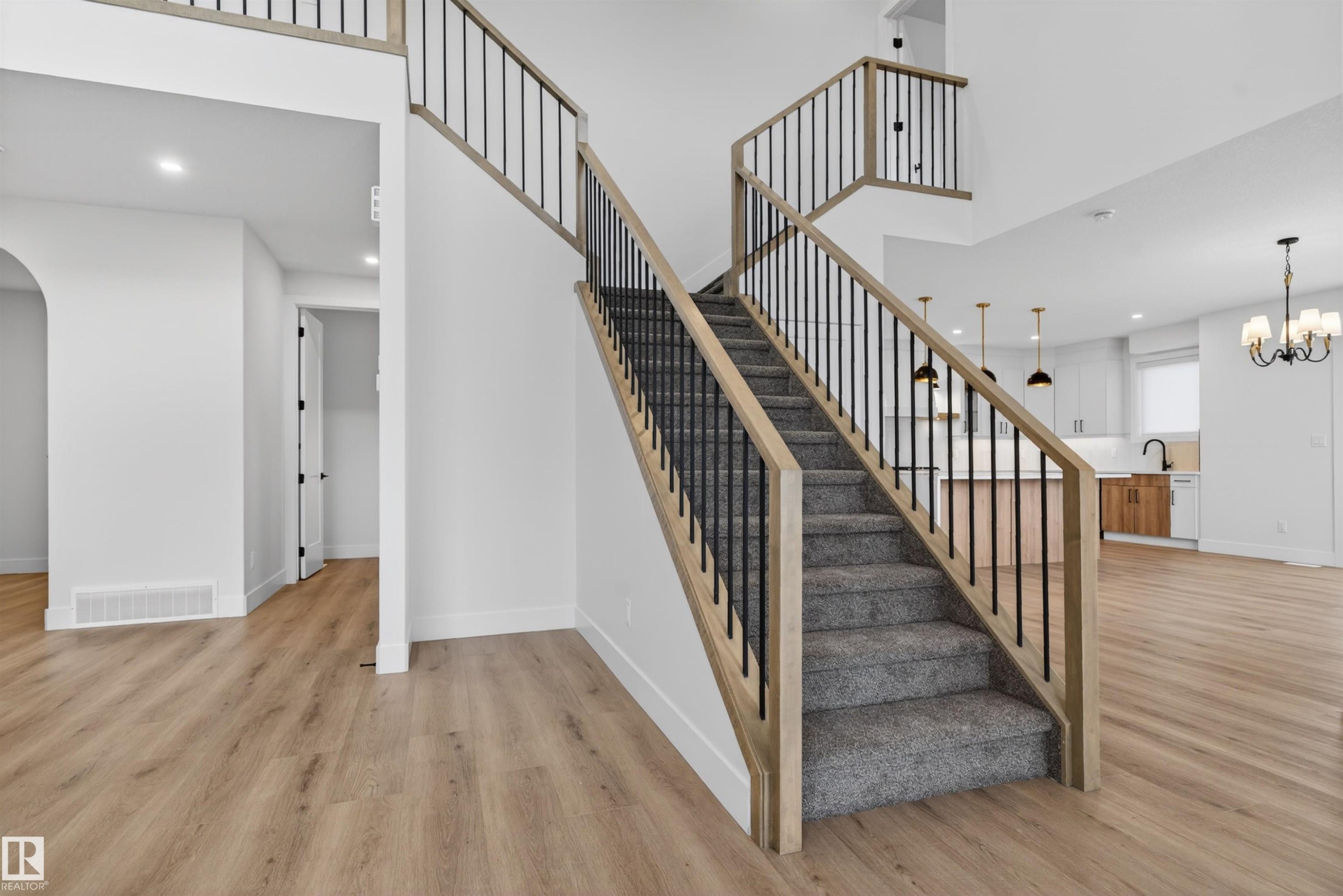Staircase featuring wood-finish railings and black balusters, carpeted treads, and light wood-finish flooring - 27 Redpoll Wynd, St. Albert, AB - Indoor Photo Showing Other Room
