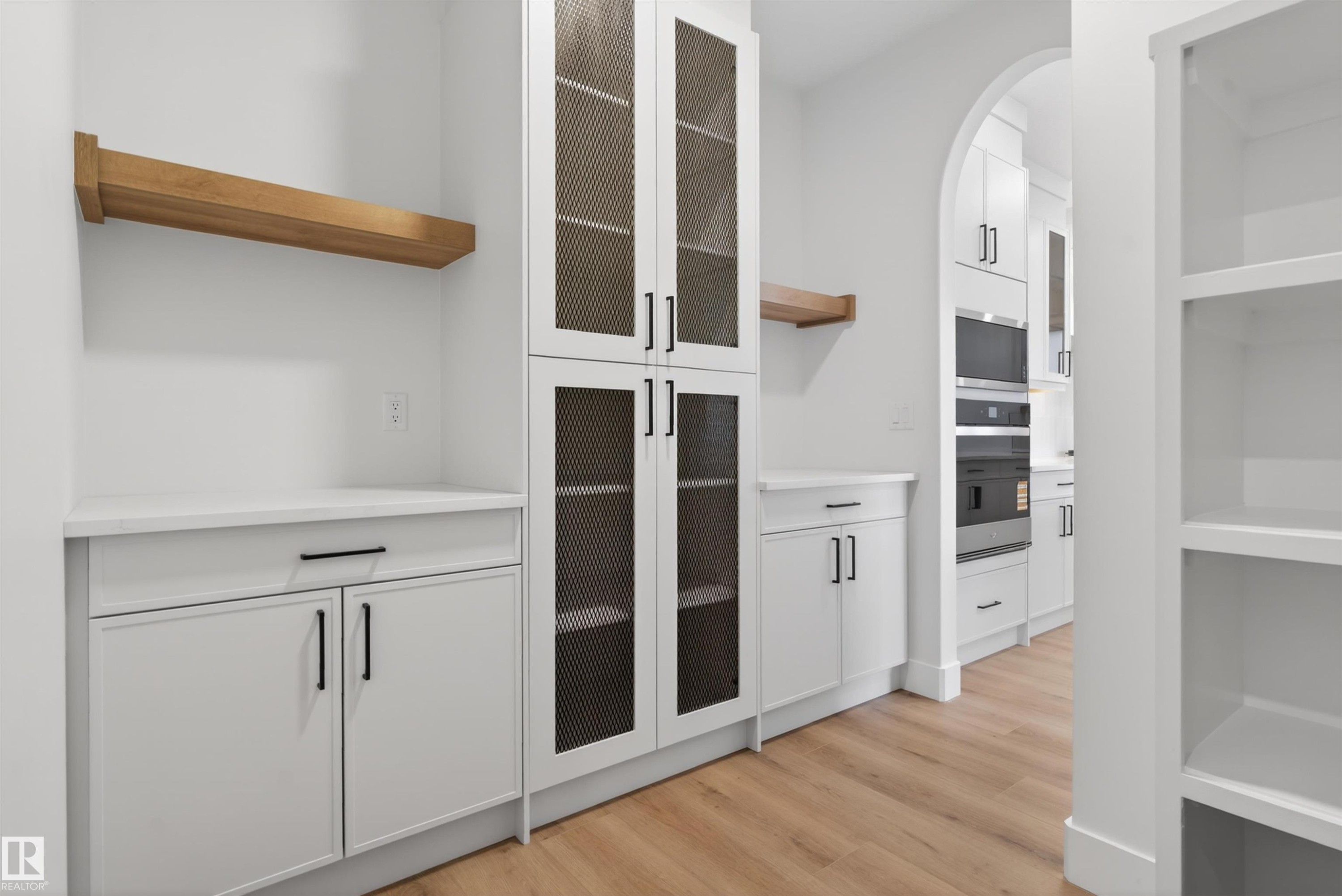 Bright space featuring wood-finish flooring, white cabinetry with matte black hardware, and an arched entryway - 27 Redpoll Wynd, St. Albert, AB - Indoor