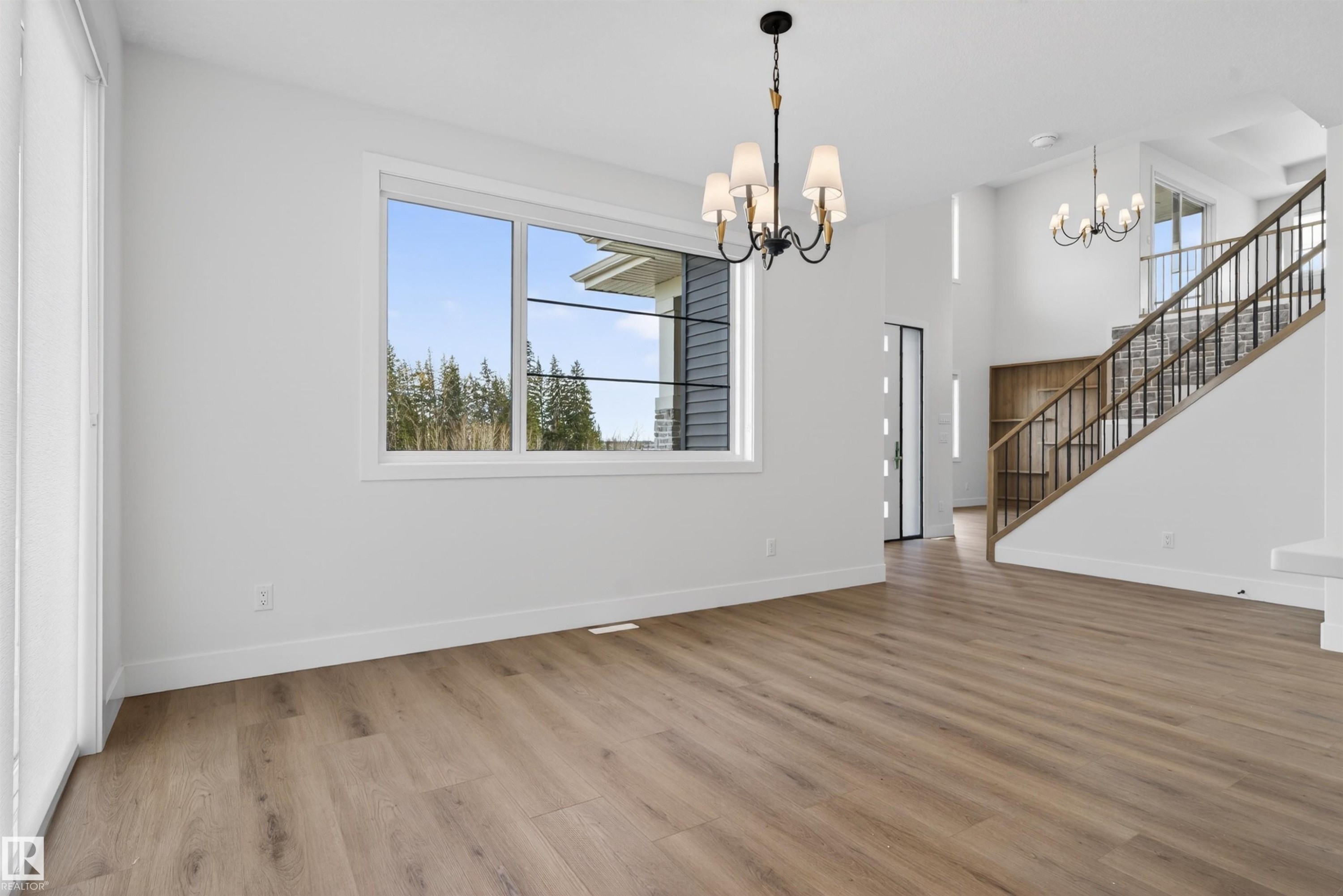 Expansive open-concept living space featuring wood-finish flooring, a large window with white trim, and a black wrought iron chandelier - 27 Redpoll Wynd, St. Albert, AB - Indoor Photo Showing Other Room