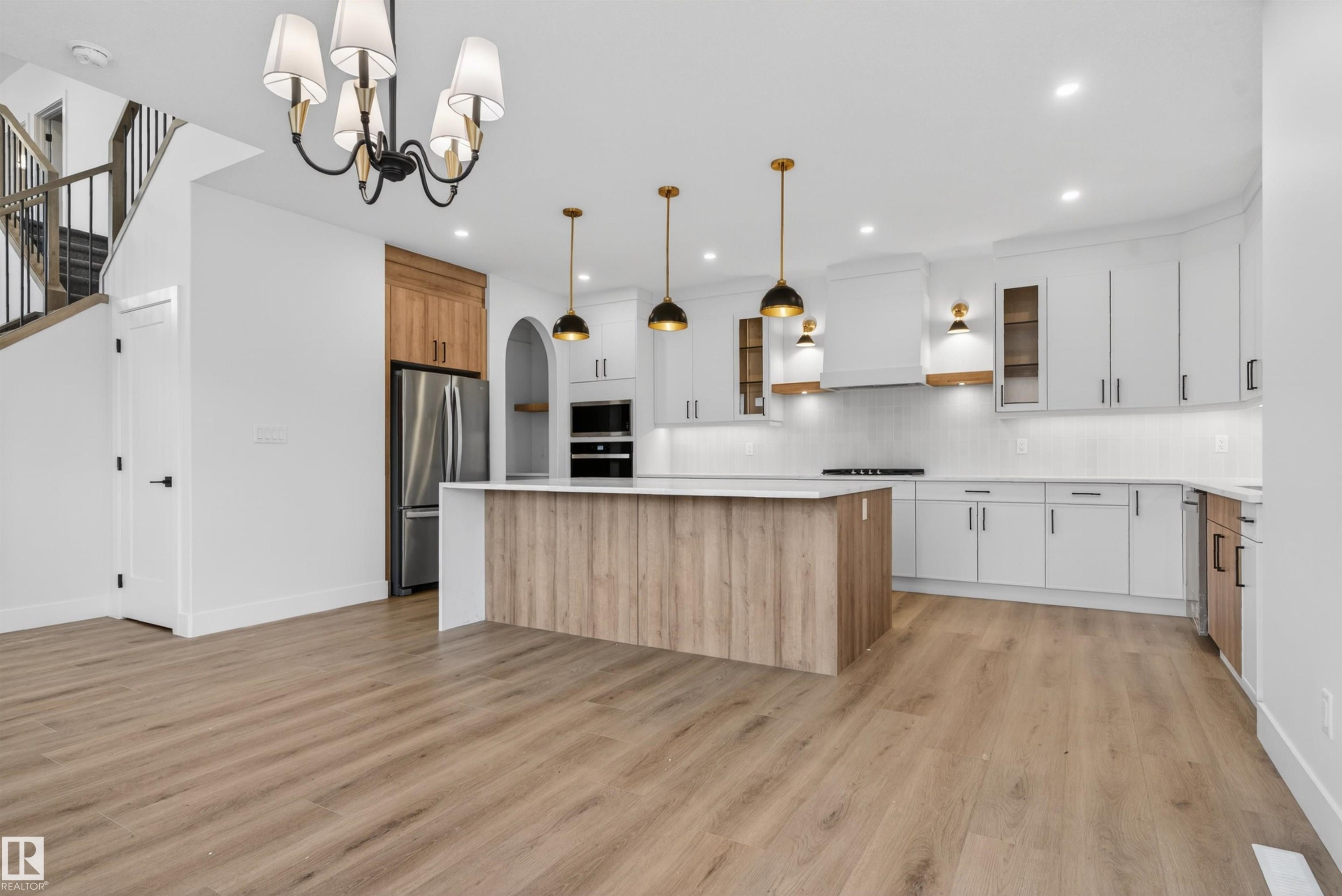 Kitchen featuring a large island with wood-finish paneling, white cabinetry, integrated stainless steel appliances, pendant lighting, and wood-finish flooring - 27 Redpoll Wynd, St. Albert, AB - Indoor Photo Showing Kitchen With Upgraded Kitchen