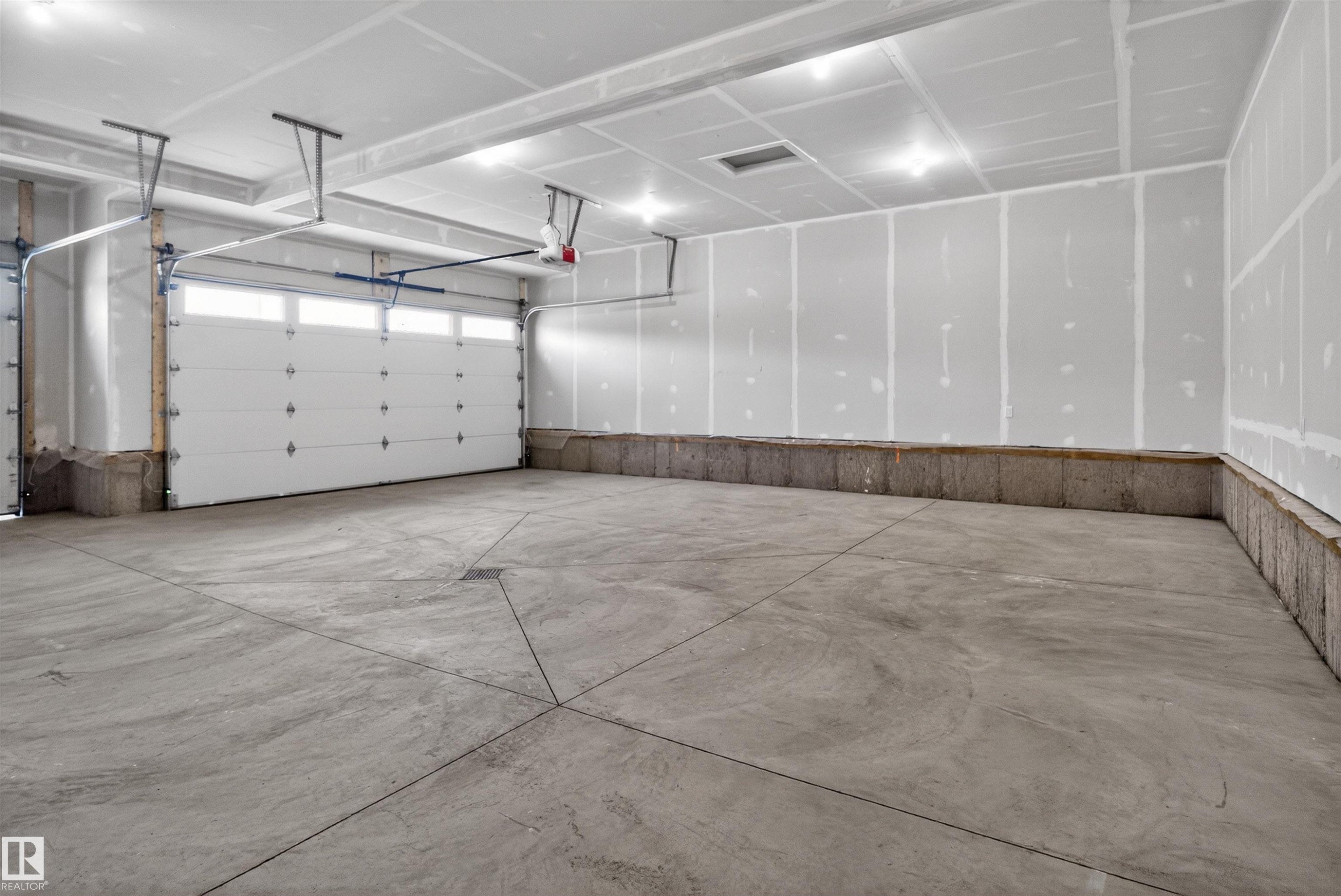 Spacious garage with exposed concrete flooring, two overhead garage doors, interior lighting, and unpainted drywall - 27 Redpoll Wynd, St. Albert, AB - Indoor Photo Showing Garage