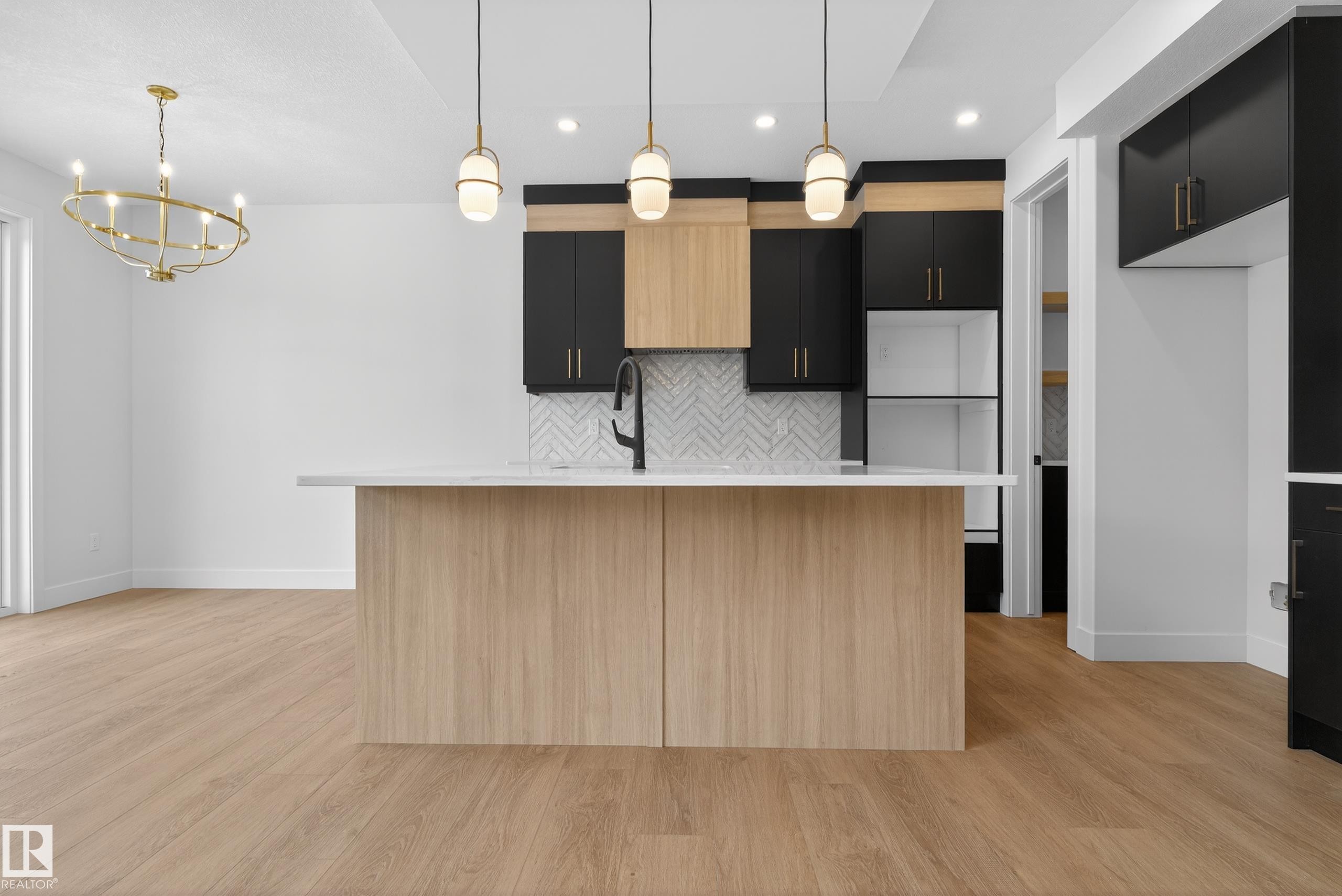 Kitchen featuring dark cabinetry, an island with sink, light wood-style flooring, and suspended lighting - 19 Rosa Crescent, St. Albert, AB - Indoor Photo Showing Kitchen