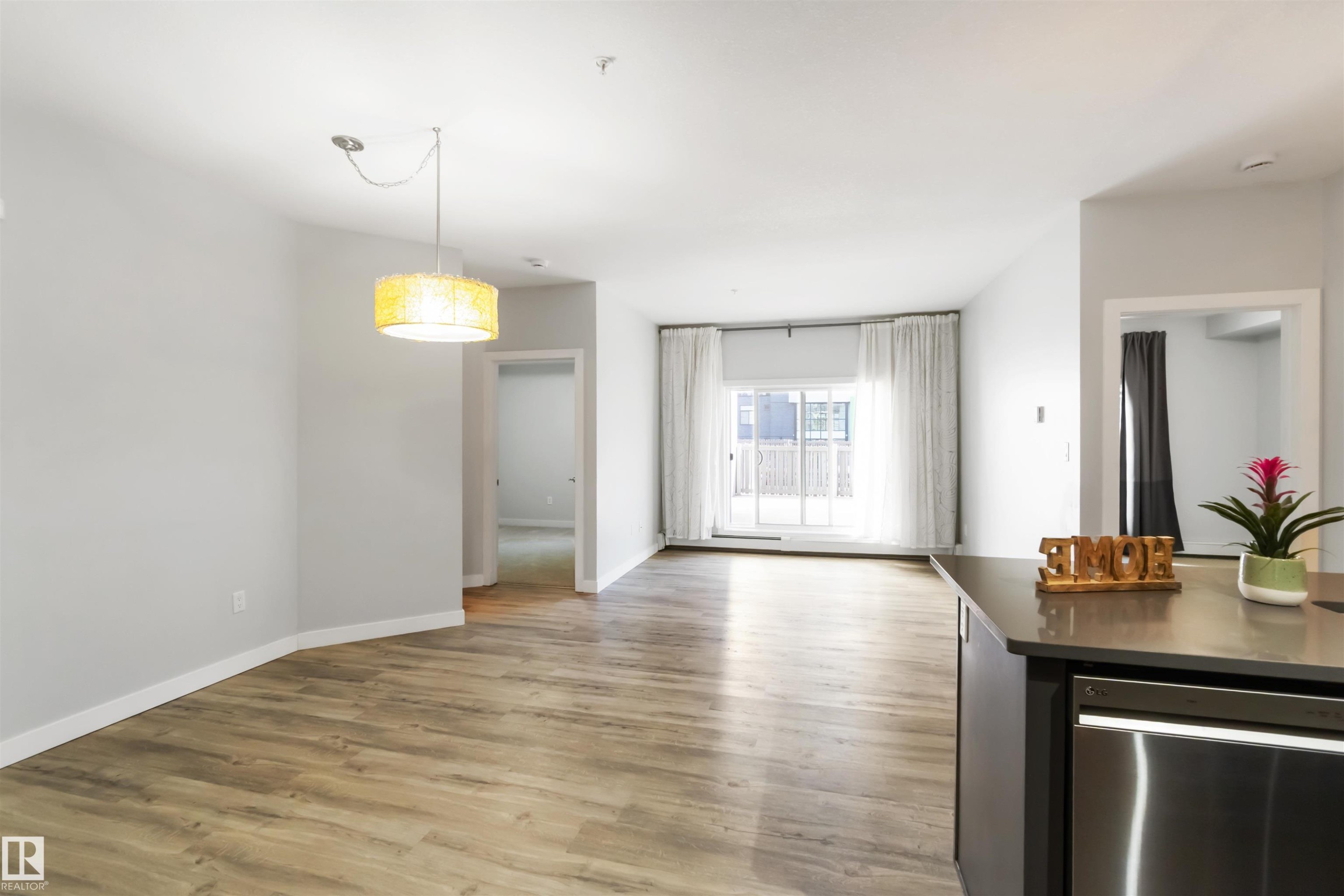 Kitchen with stainless steel dishwasher, light wood finished floors, hanging light fixtures, dark countertops, and open floor plan - 107 10611 117 Street, Edmonton, AB - Indoor