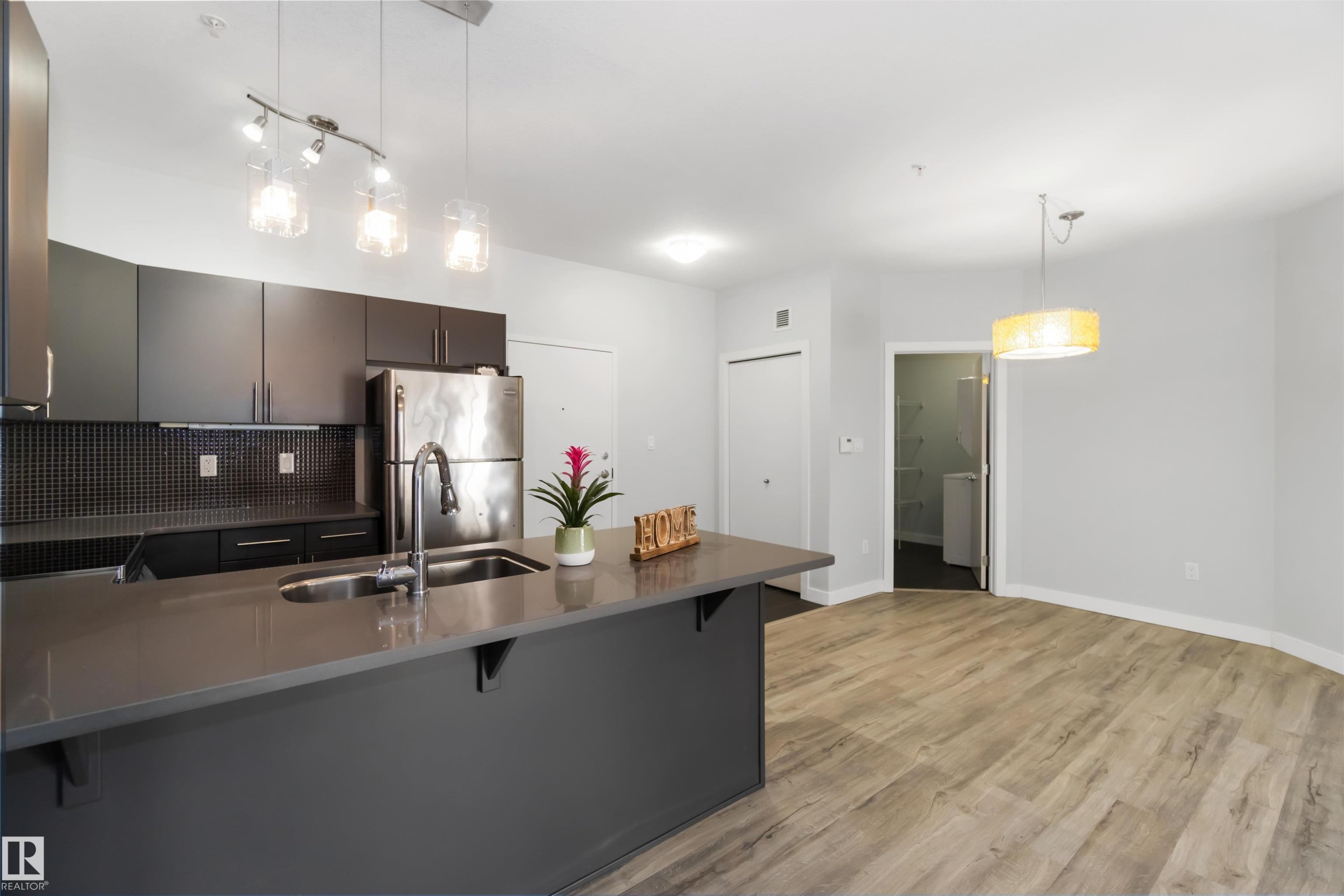Kitchen with a breakfast bar, a peninsula, hanging light fixtures, light wood finished floors, and decorative backsplash - 107 10611 117 Street, Edmonton, AB - Indoor Photo Showing Kitchen With Double Sink With Upgraded Kitchen