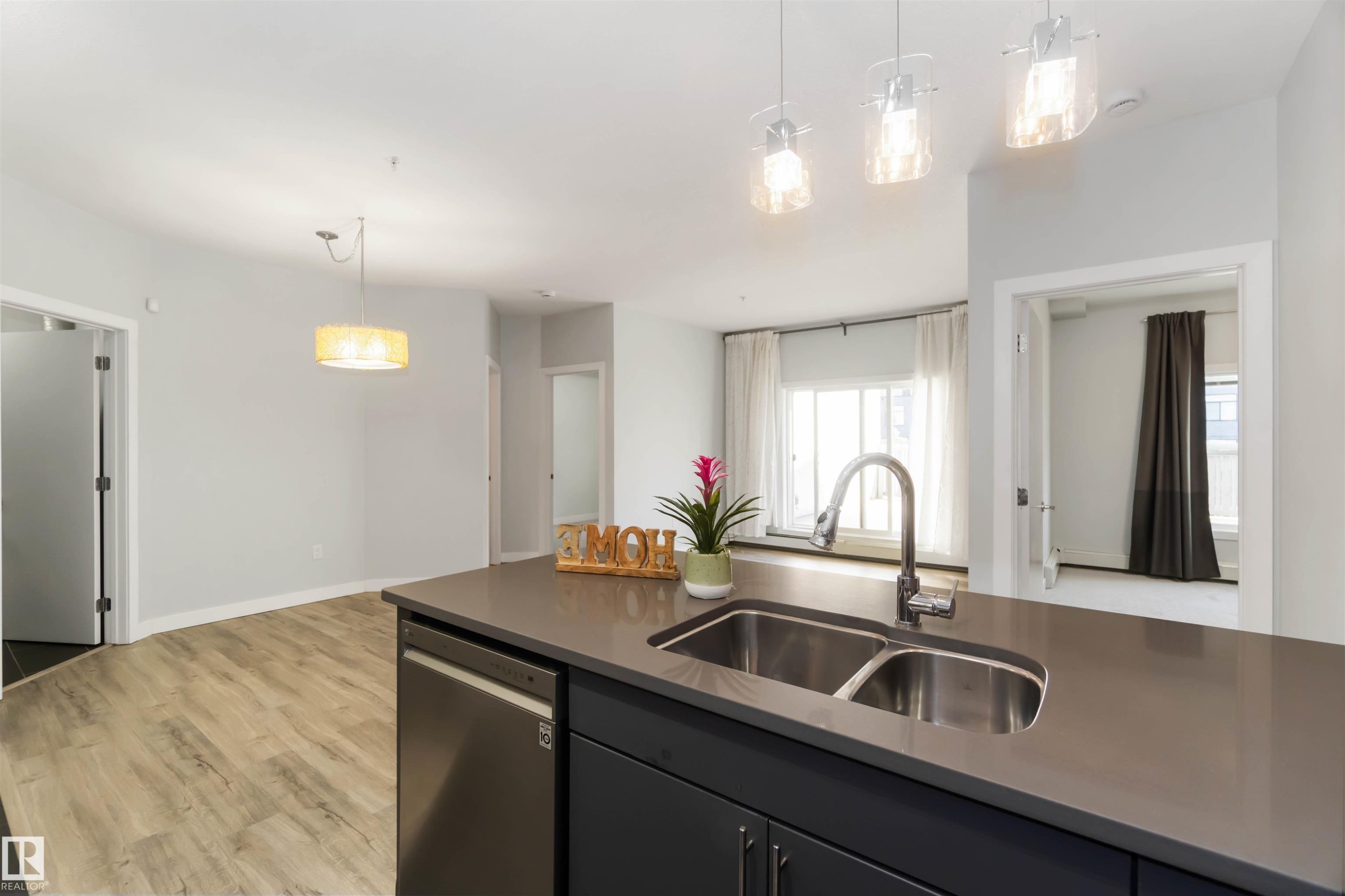 Kitchen featuring hanging light fixtures, stainless steel dishwasher, and light wood-style flooring - 107 10611 117 Street, Edmonton, AB - Indoor Photo Showing Kitchen With Double Sink