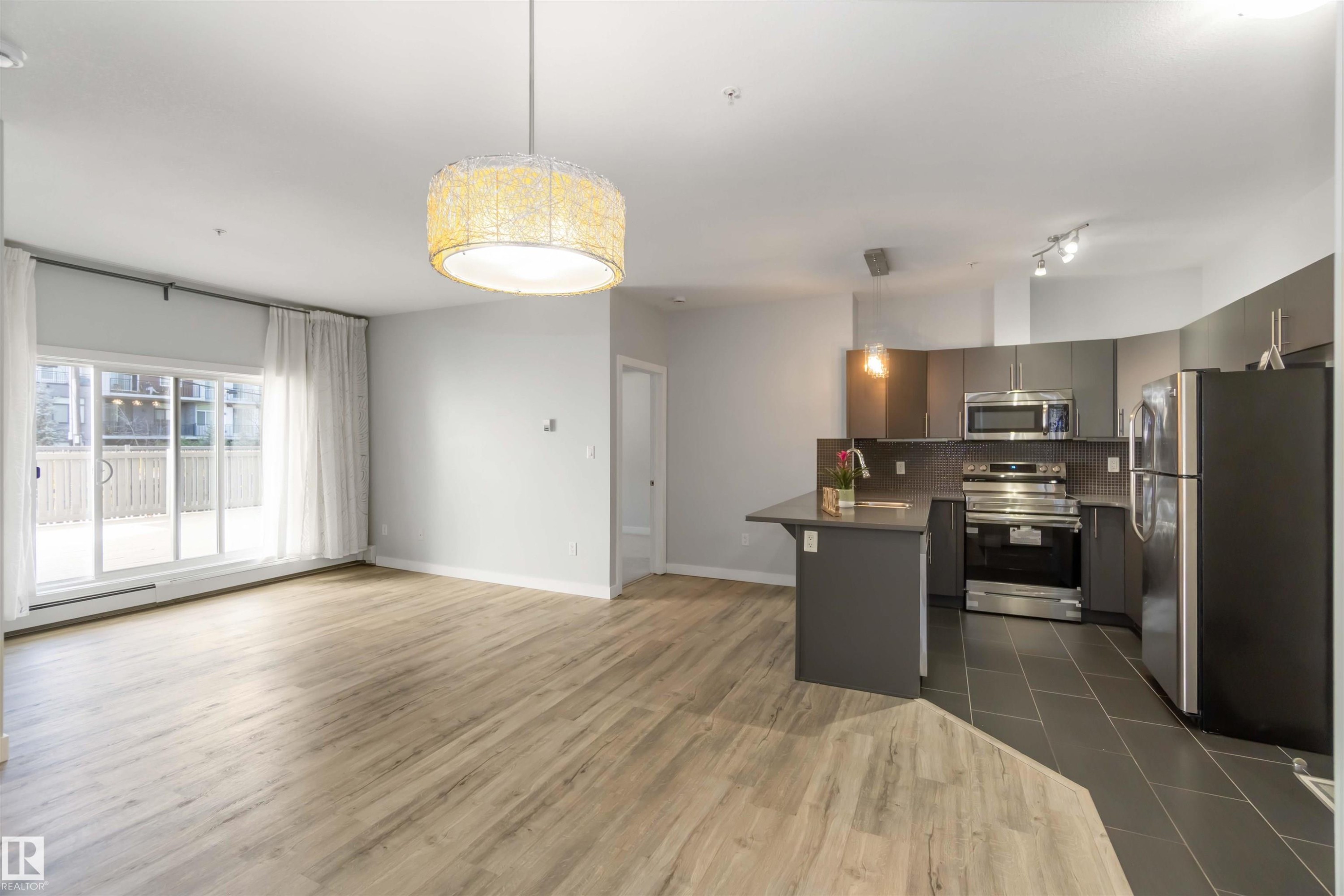 Kitchen featuring appliances with stainless steel finishes, open floor plan, pendant lighting, and gray cabinets - 107 10611 117 Street, Edmonton, AB - Indoor Photo Showing Kitchen
