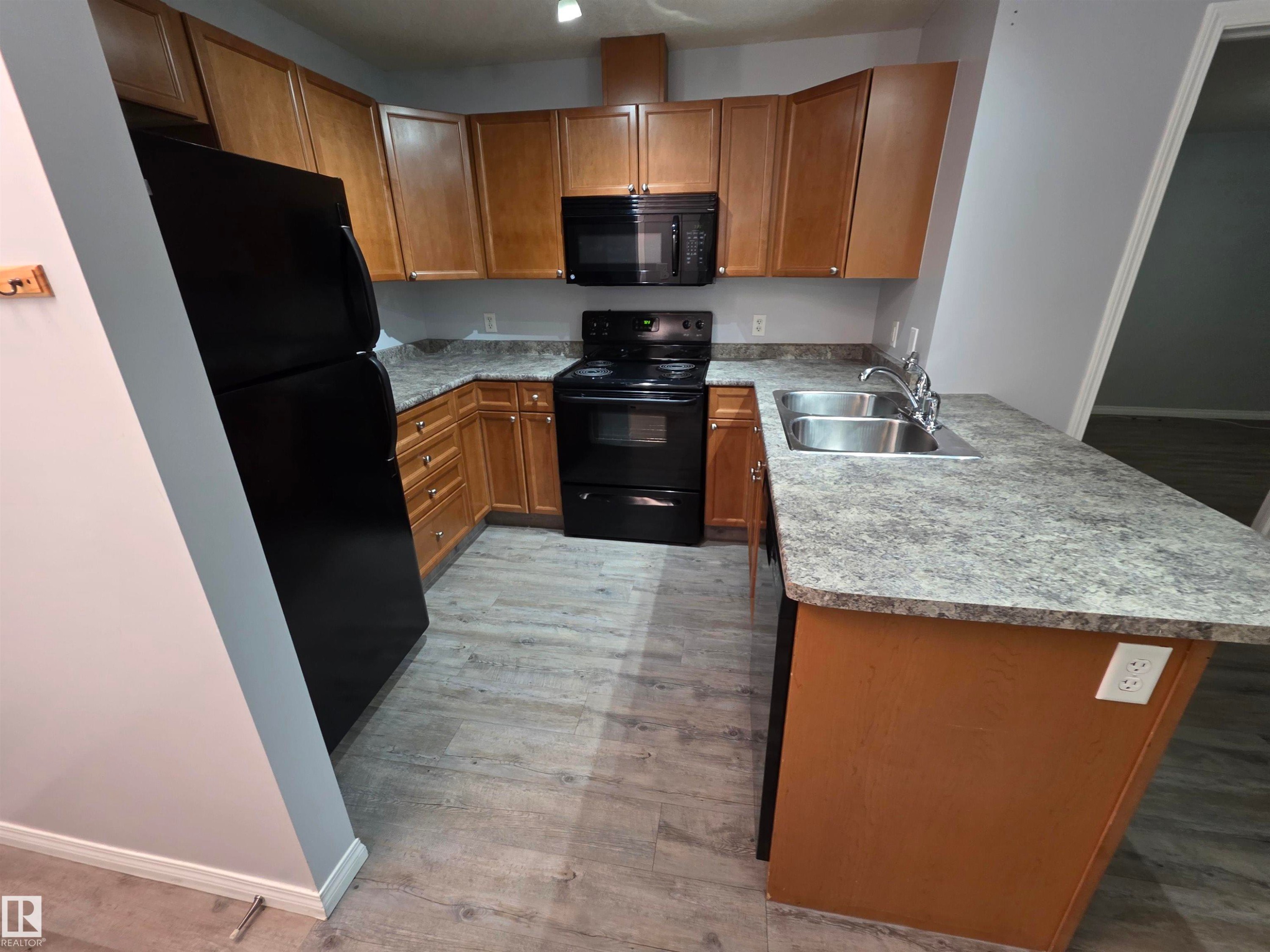 Kitchen featuring black appliances, brown cabinets, a peninsula, light countertops, and light wood-style floors - 106 4903 47 Avenue, Stony Plain, AB - Indoor Photo Showing Kitchen With Double Sink