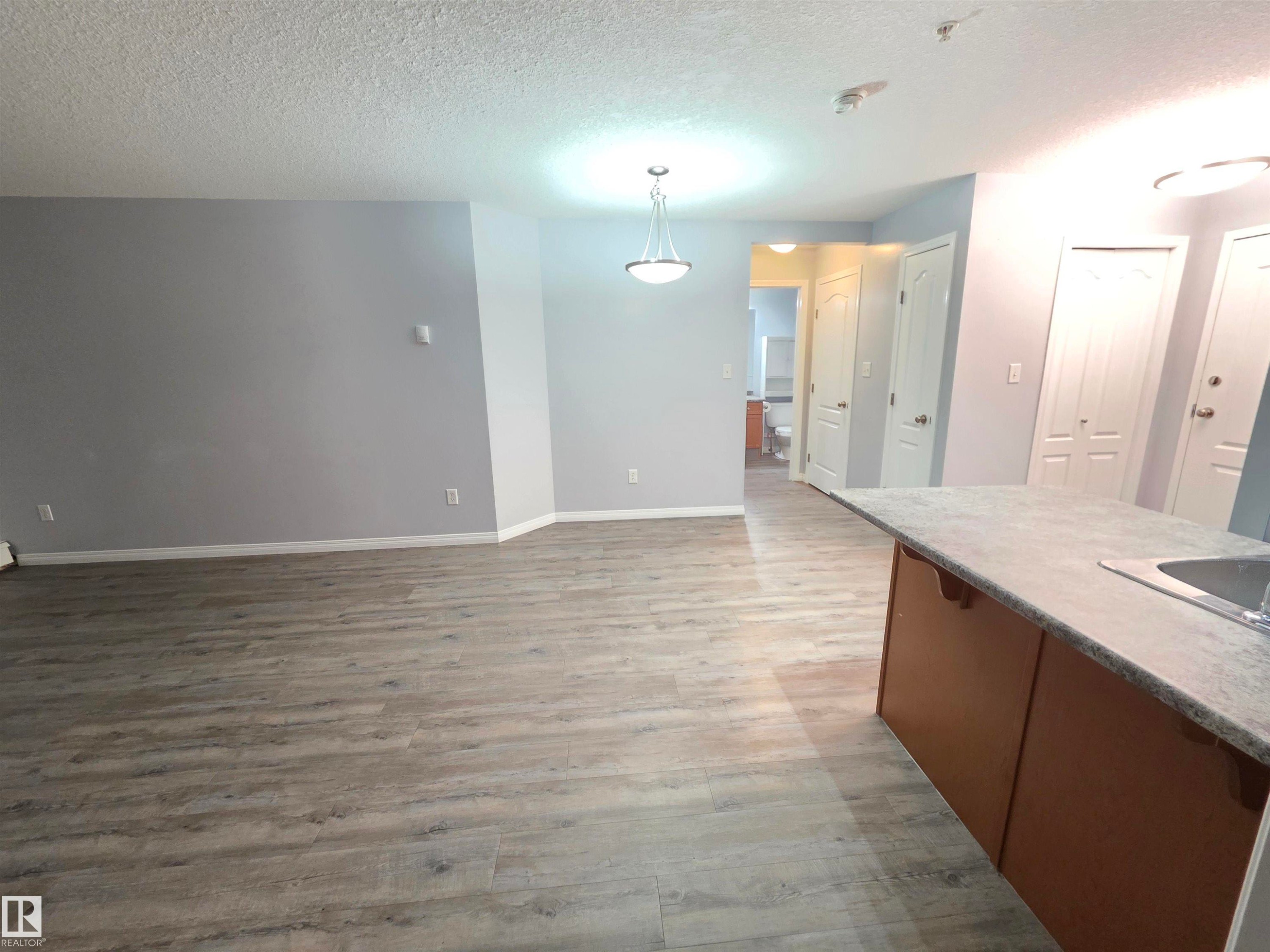 Kitchen featuring a textured ceiling, light wood-style flooring, pendant lighting, open floor plan, and light countertops - 106 4903 47 Avenue, Stony Plain, AB - Indoor