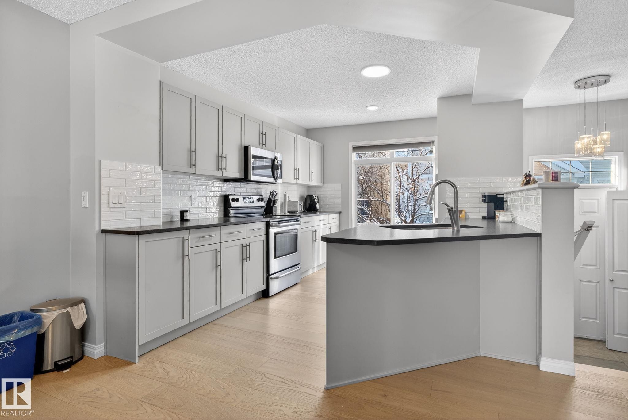 Kitchen featuring a textured ceiling, stainless steel appliances, a peninsula, light wood-style floors, and pendant lighting - 60 1804 70 Street, Edmonton, AB - Indoor Photo Showing Kitchen With Upgraded Kitchen